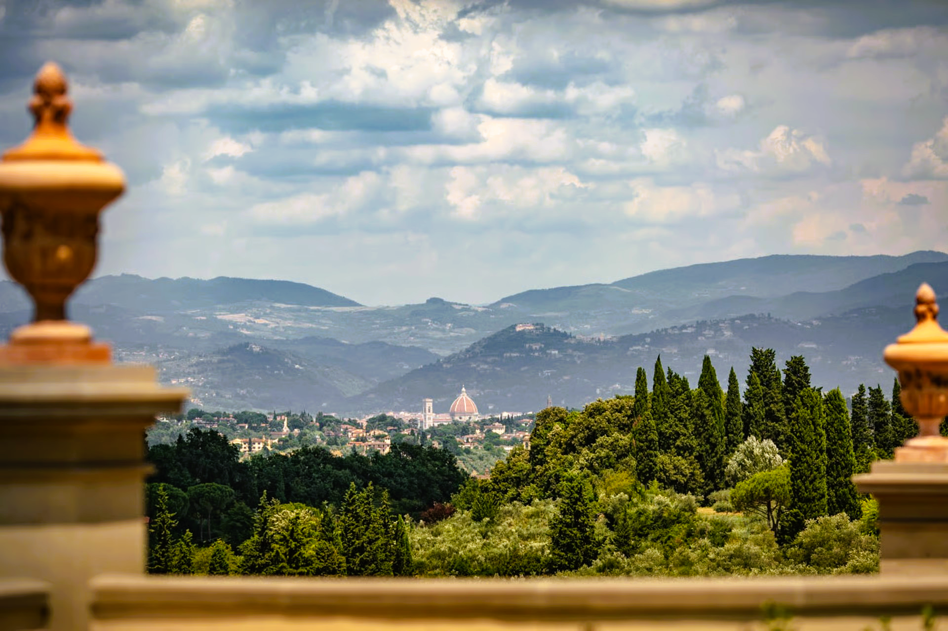 Scenic view of Florence, Italy, with hills, trees, and a dome, framed by ornamental urns.