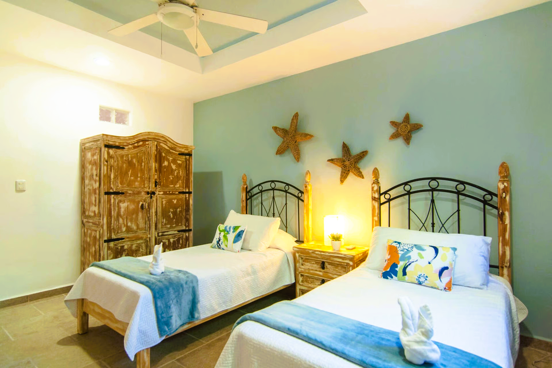 Bedroom with two twin beds, blue and white decor, starfish wall art, light wood wardrobe.