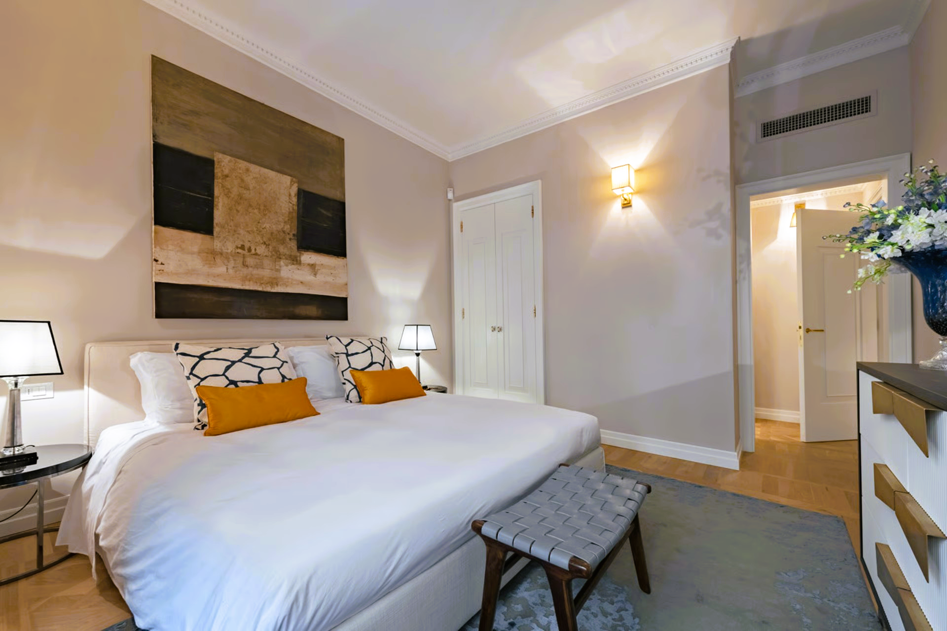 Bedroom with king bed, art, bench, nightstands, and an open door to another room.