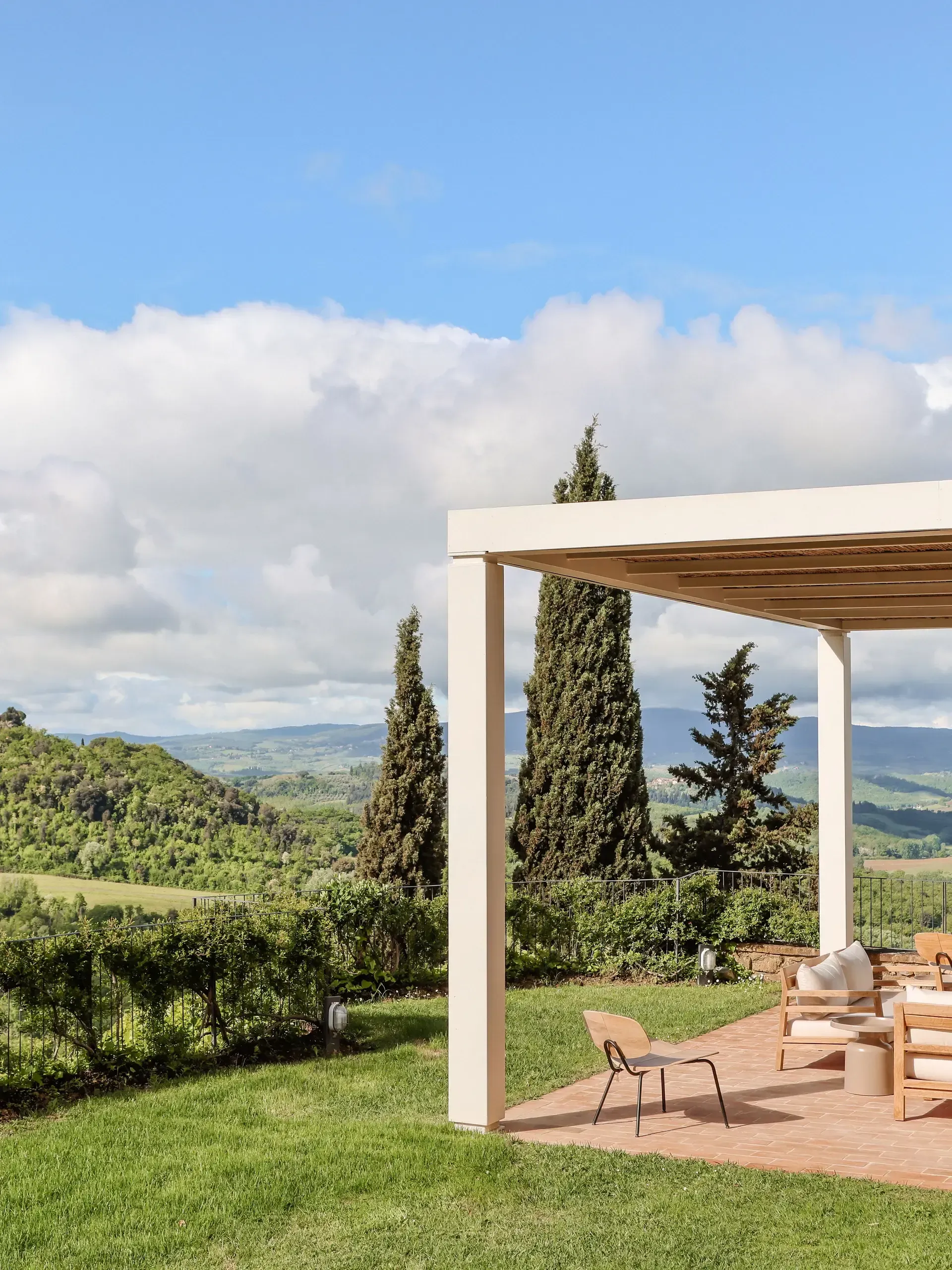 Patio with a pergola overlooking a rolling green landscape under a partly cloudy sky.