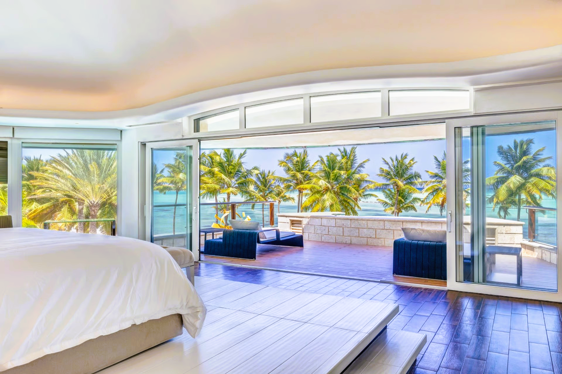 Spacious bedroom with open doors to a patio overlooking the ocean and palm trees.