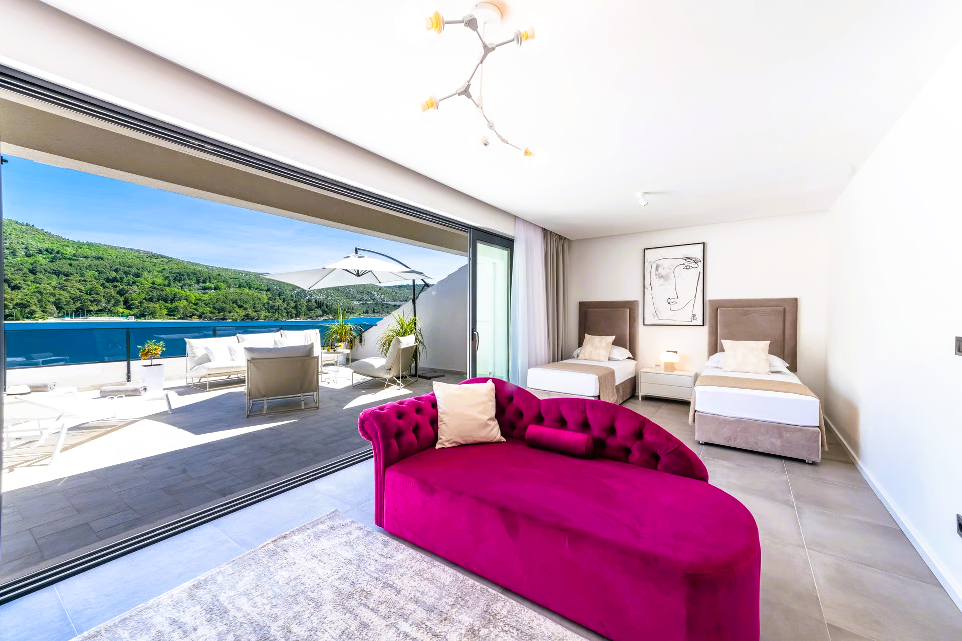 A luxury bedroom with water view: pink chaise lounge, three beds, and open sliding door to patio.
