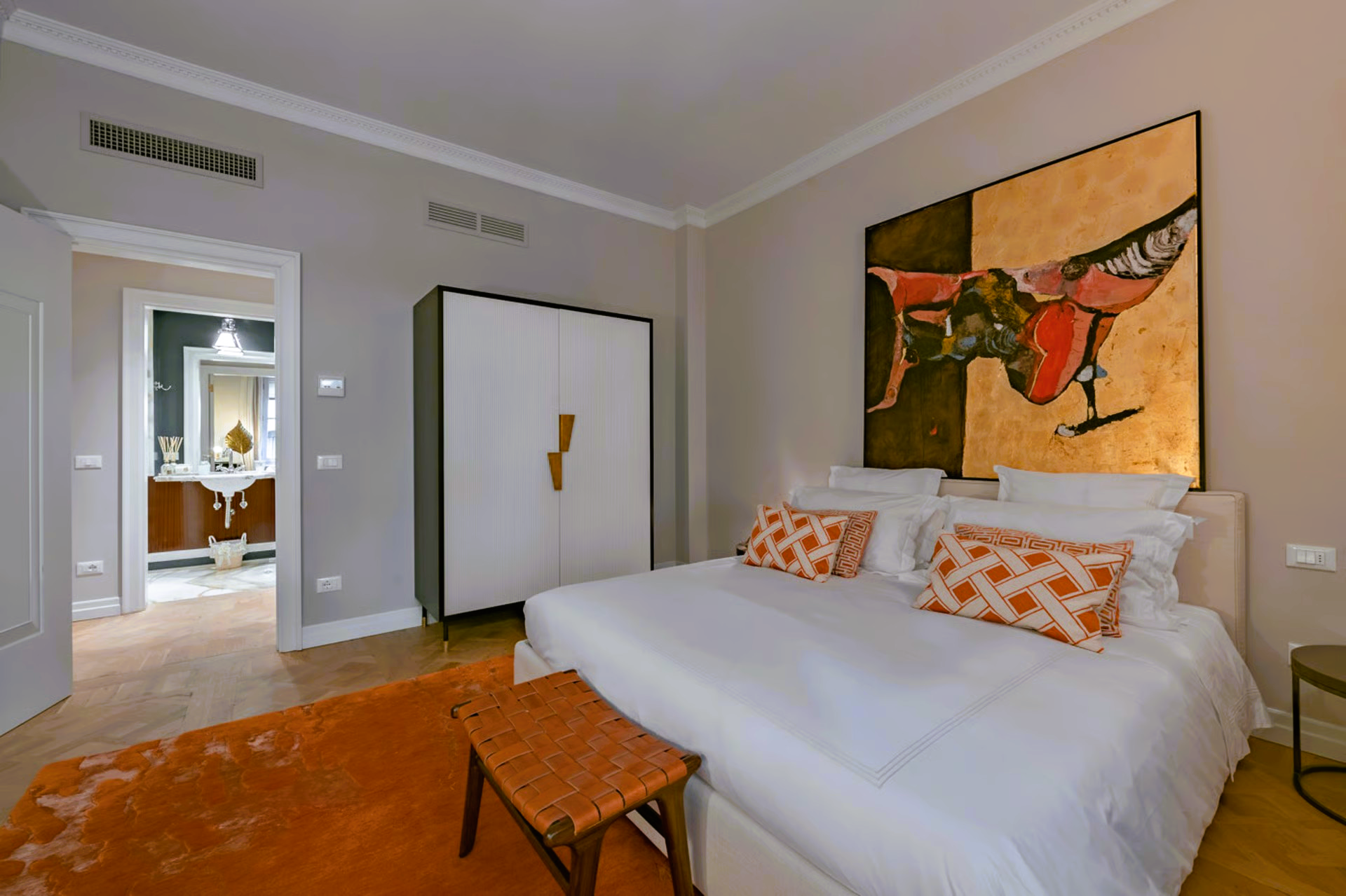 Bedroom with orange accents. Bed, wardrobe, artwork on wall. Bathroom visible in the doorway.