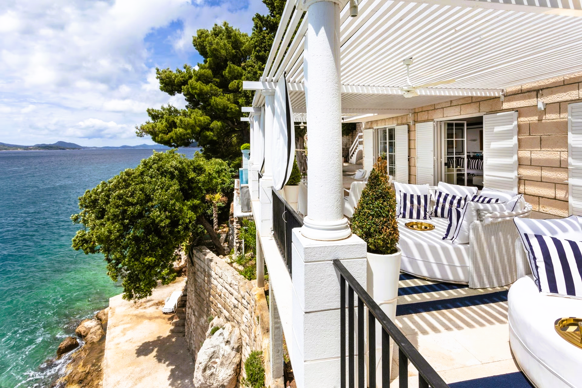 Oceanfront patio with white pergola, striped cushions, and turquoise water.