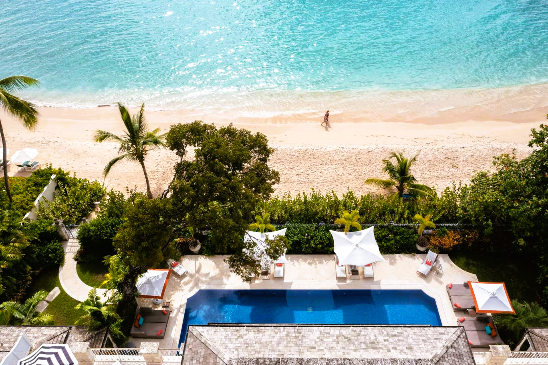 Overhead view of a luxury resort with a turquoise ocean, beach, swimming pool, and lush greenery.