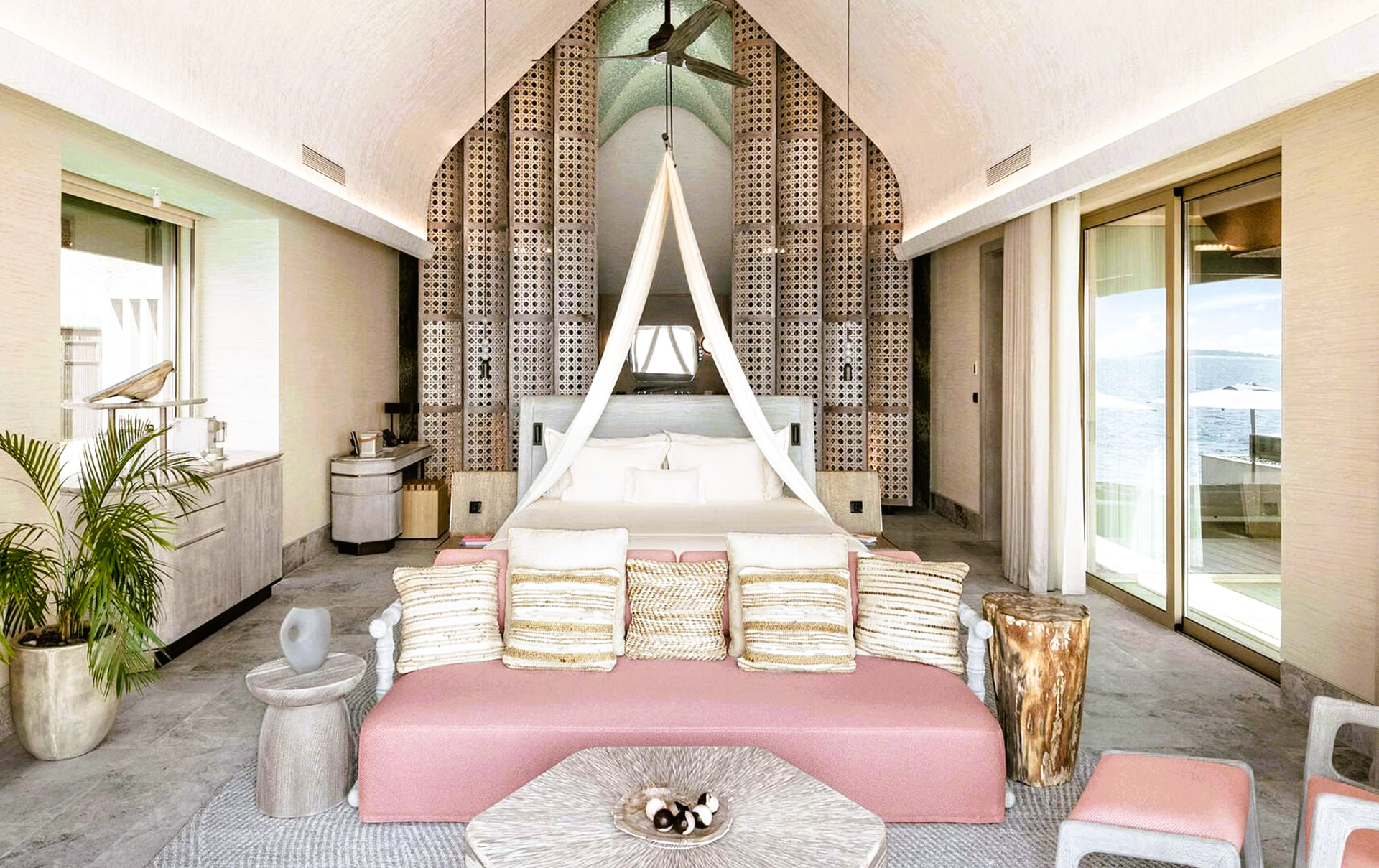 Spacious hotel bedroom with a pink couch, canopy bed, and ocean view.