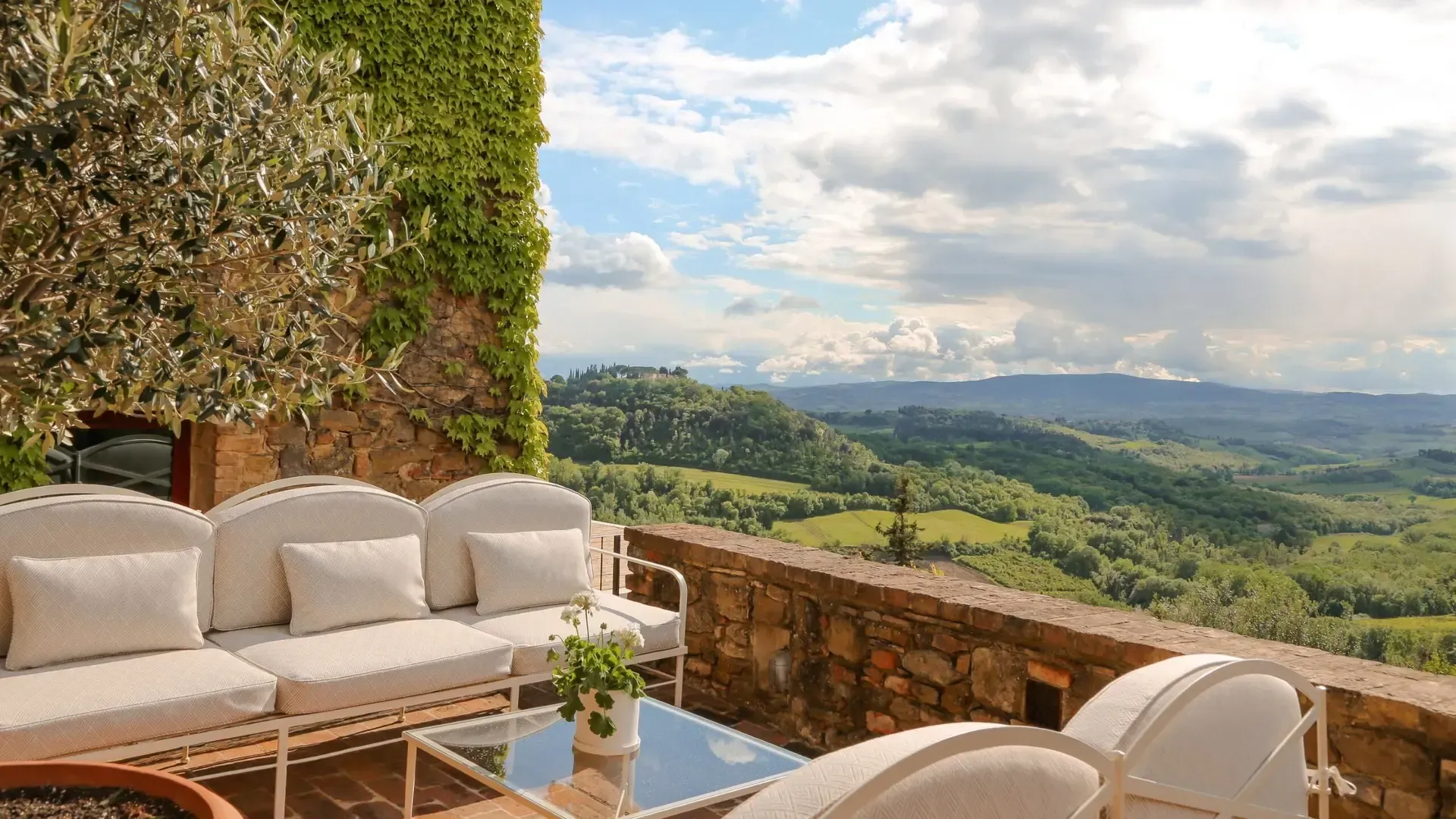 Terrace with white sofas, overlooking rolling green hills and cloudy sky.