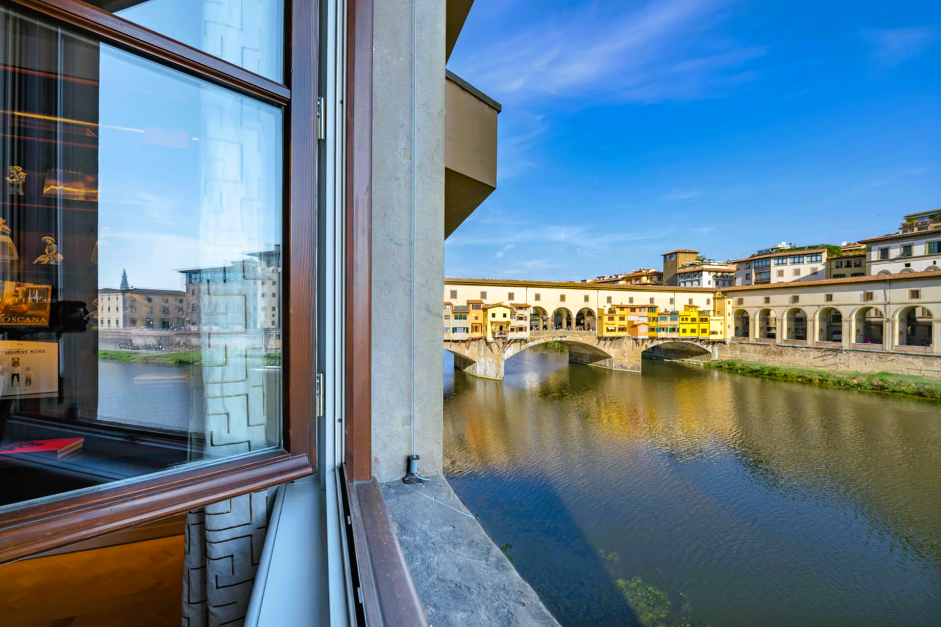 View from a window of the Ponte Vecchio bridge over the Arno River in Florence, Italy, on a sunny day.