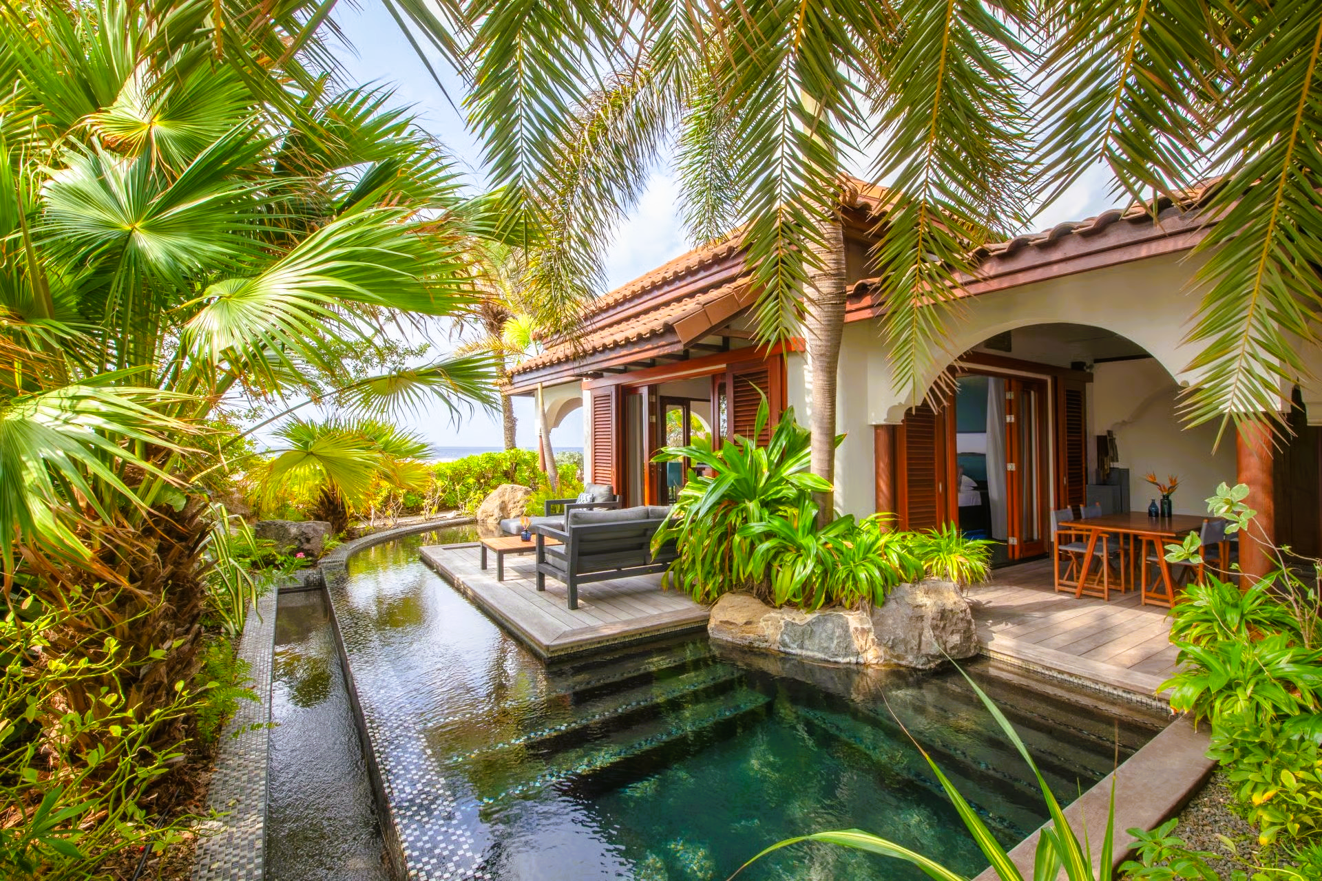 Tropical villa with a pool, lush greenery, and ocean view.