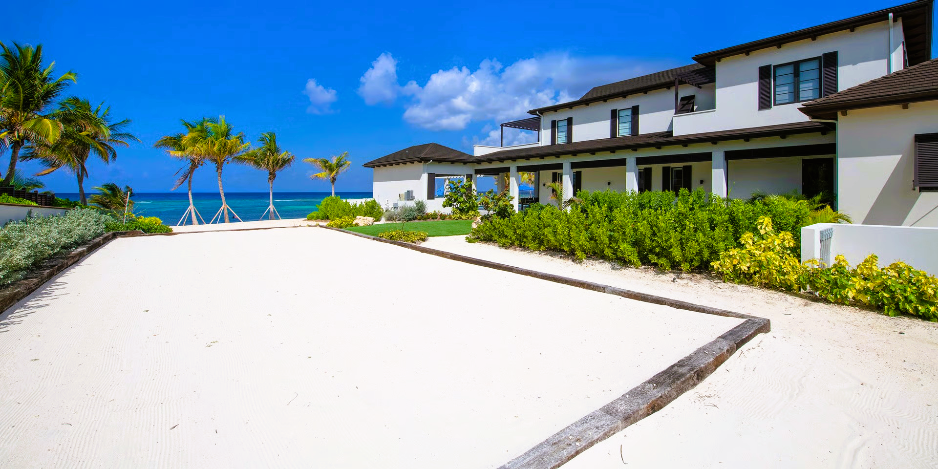 A white house on a sandy beach with palm trees and a clear blue sky.