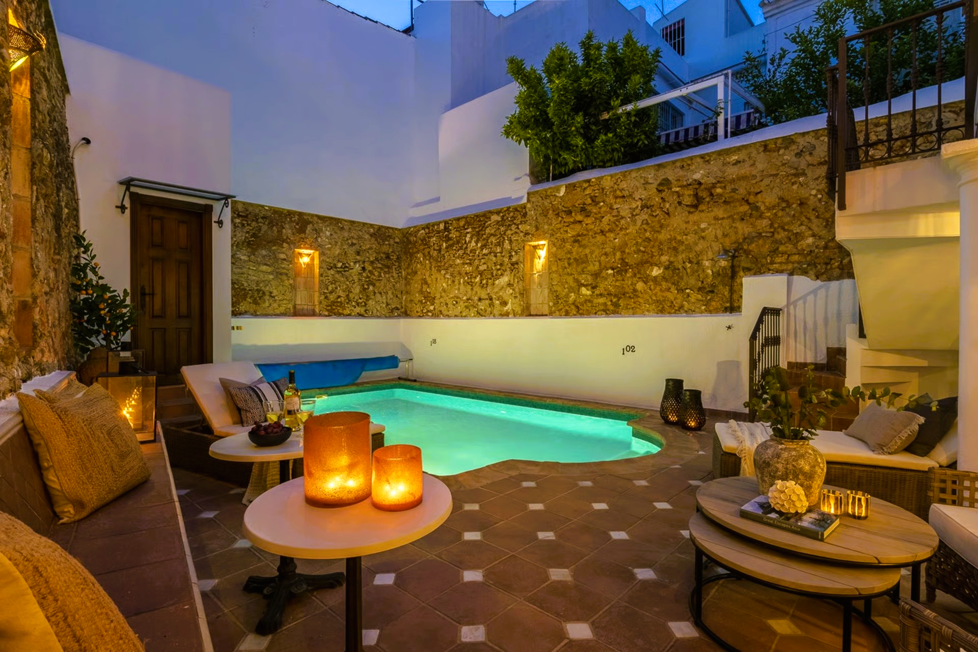 Cozy outdoor patio with a pool and seating. Warm lighting, white walls, and a stone accent wall.