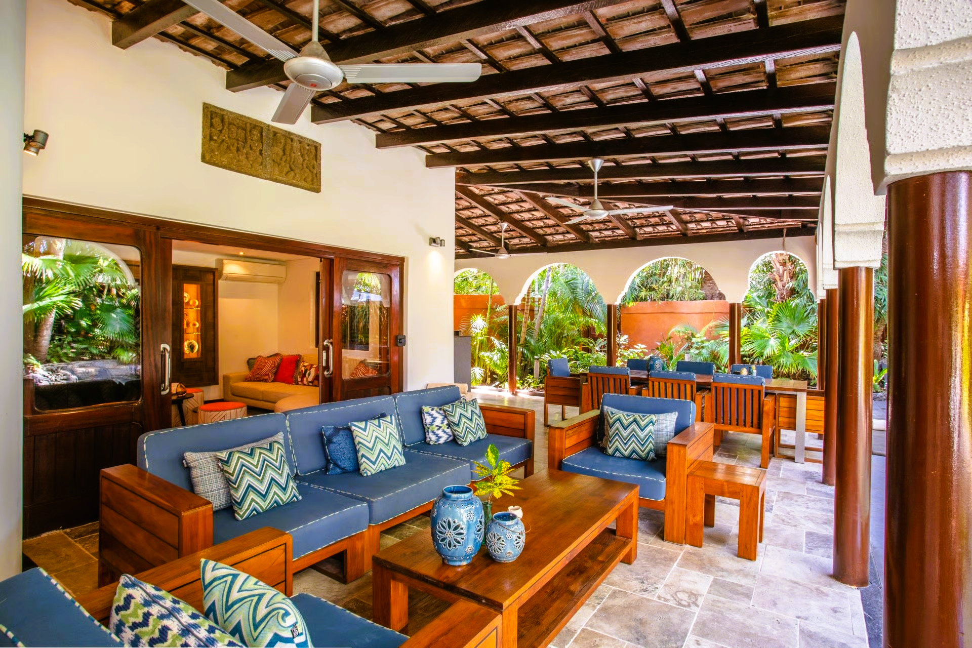 Outdoor living area with blue couches, wooden furniture, and lush greenery.