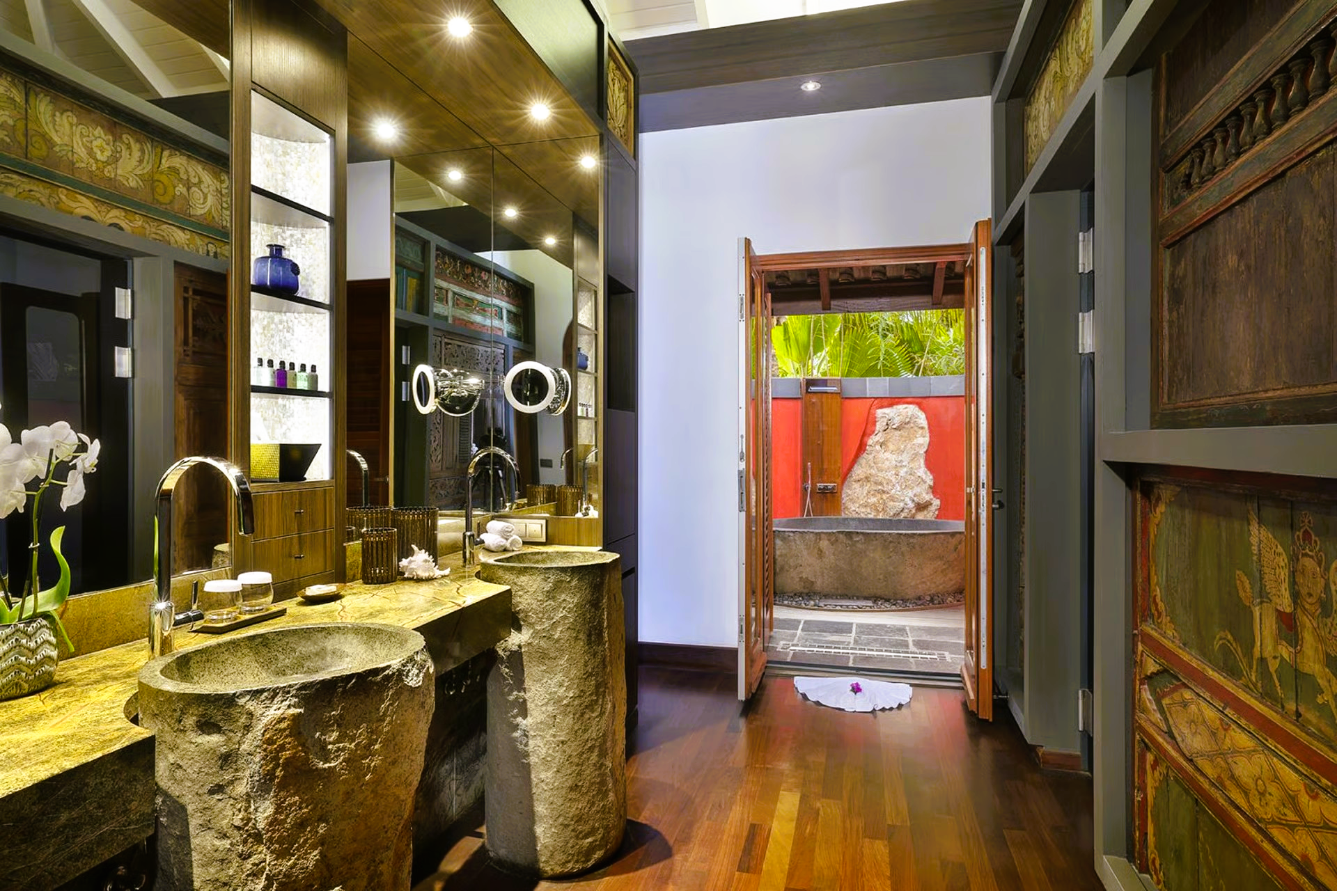 Luxurious bathroom with stone sinks, ornate wood details, and a glimpse of an outdoor garden.
