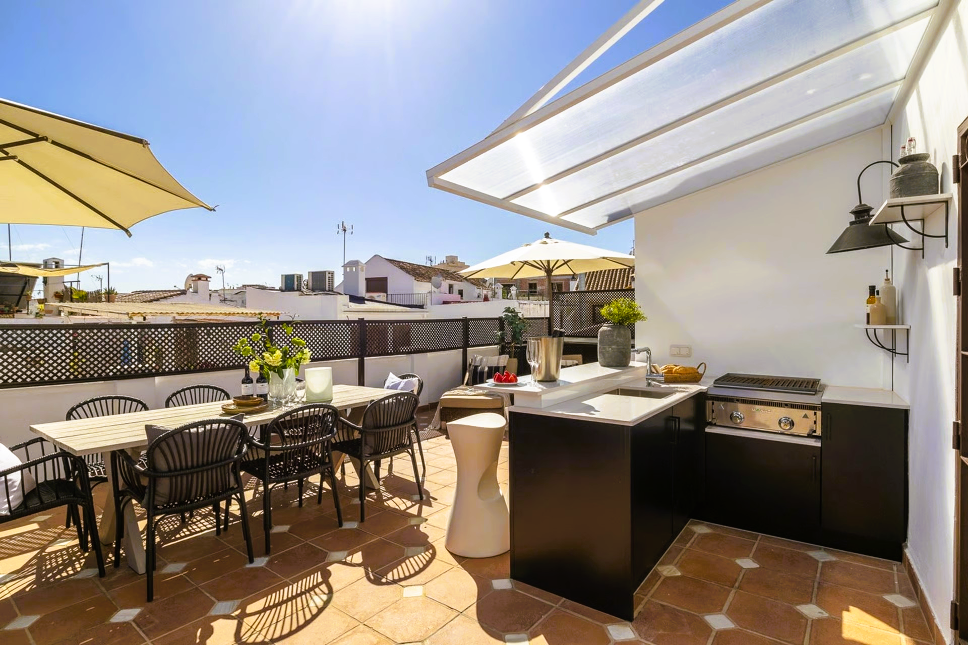 Rooftop patio with dining area, outdoor kitchen, and partial sun shade, bathed in sunlight.