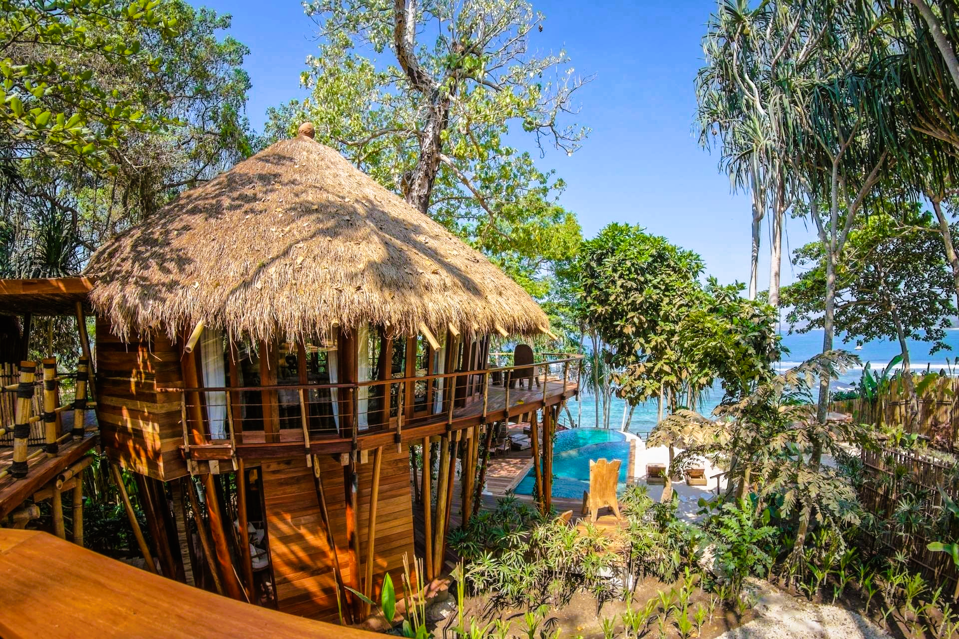 Wooden treehouse with thatched roof overlooking the ocean.