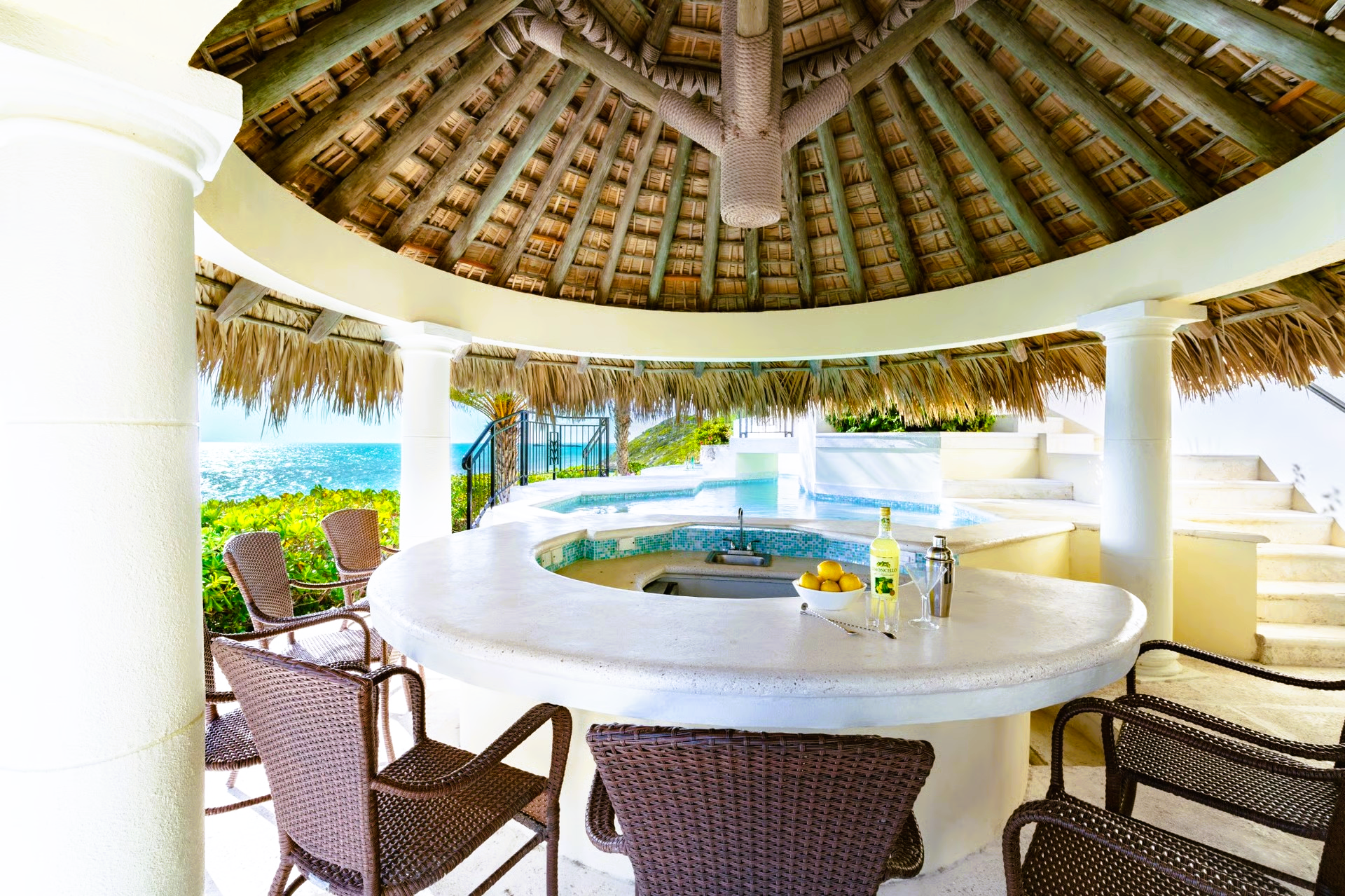 Tropical outdoor bar with thatched roof, white counter, and ocean view.