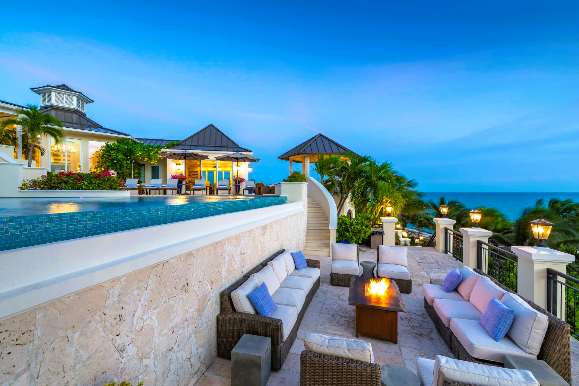 Luxury outdoor patio with ocean view, couches, fire pit, and pool.