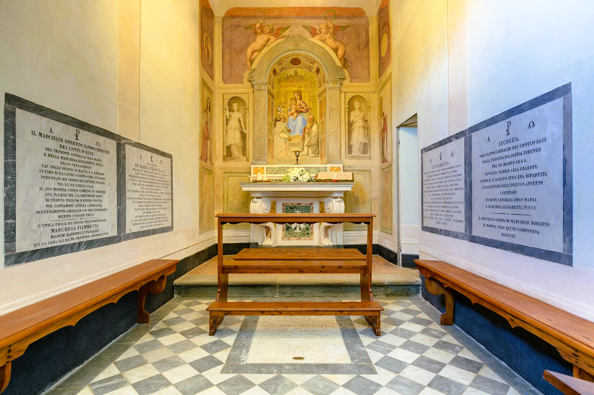 Inside a chapel, a painting of Mary and Jesus, benches, marble flooring, and stone inscriptions.