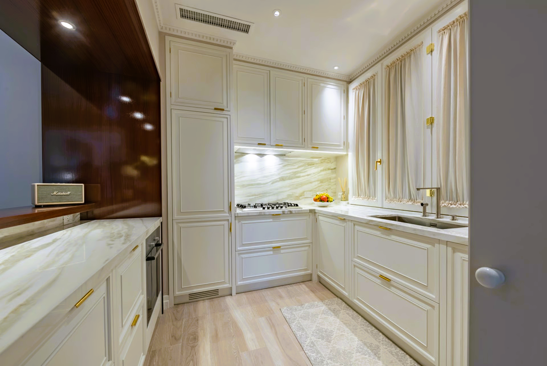 Small, elegant white kitchen with marble counters, cabinets, and a curtained window.