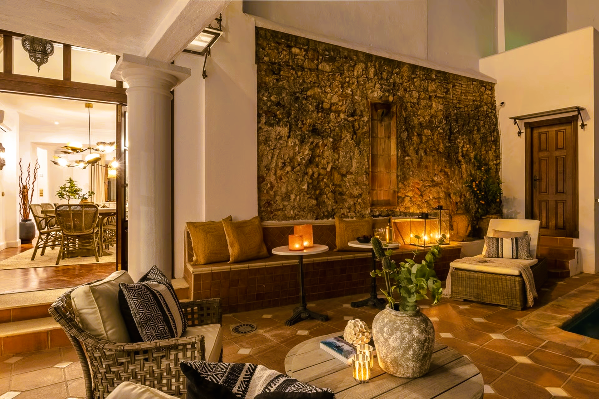 Cozy outdoor patio with seating, warm lighting, and a textured stone wall with a fireplace.