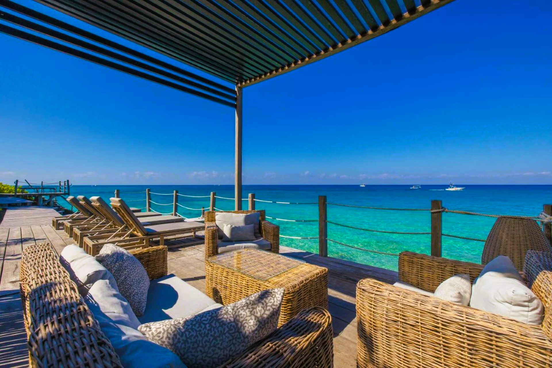 Outdoor patio overlooking turquoise ocean; wicker furniture, blue sky.
