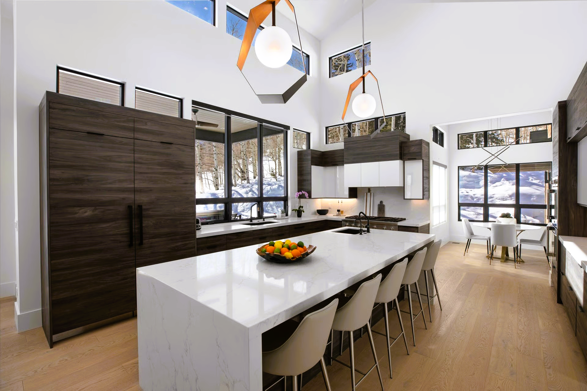 Modern kitchen with large island, white countertop, wood cabinets, and snow-covered outdoor view.