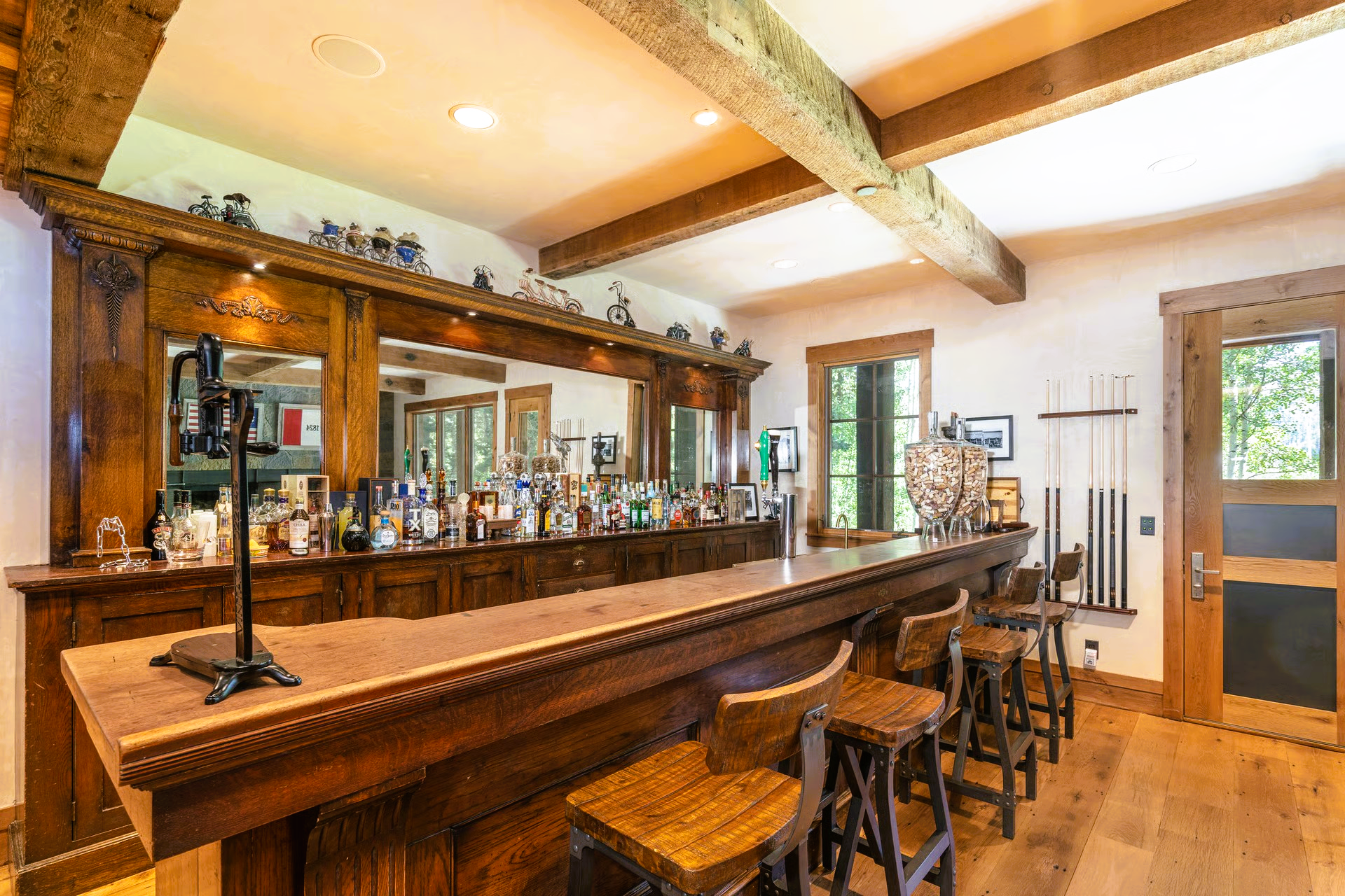 Rustic wooden bar with stools, liquor bottles, and mirrored back, in a room with wood beams.