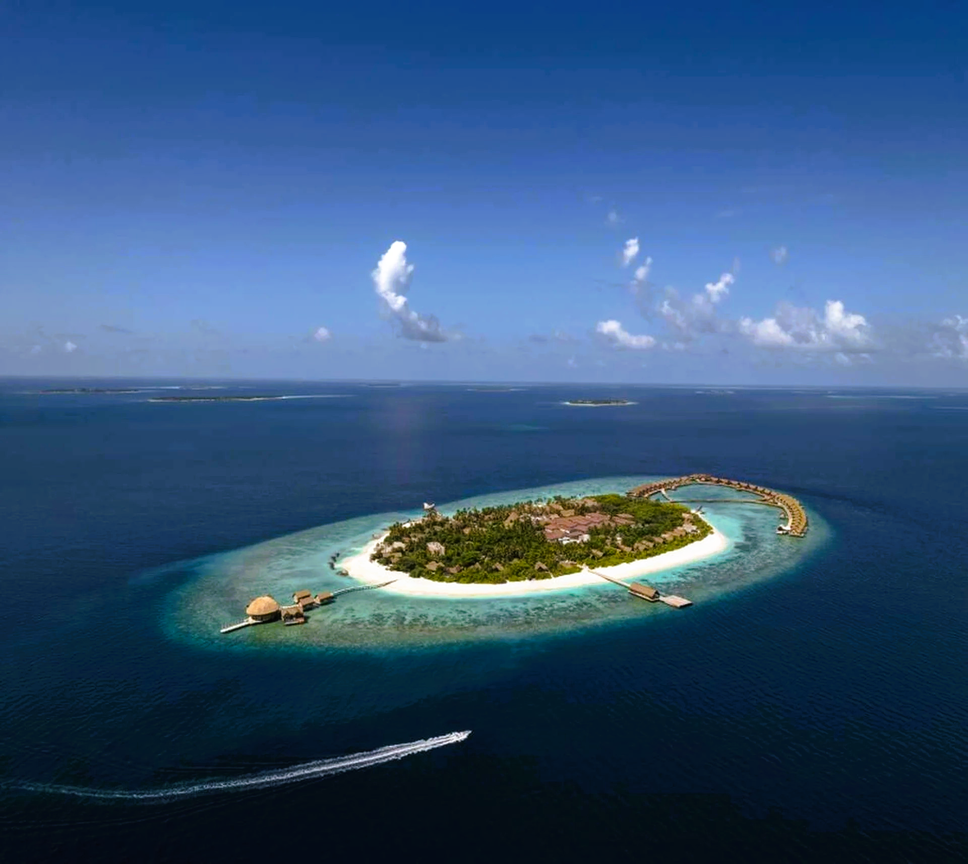 Island resort in turquoise waters with clear sky. A boat leaves a white wake.