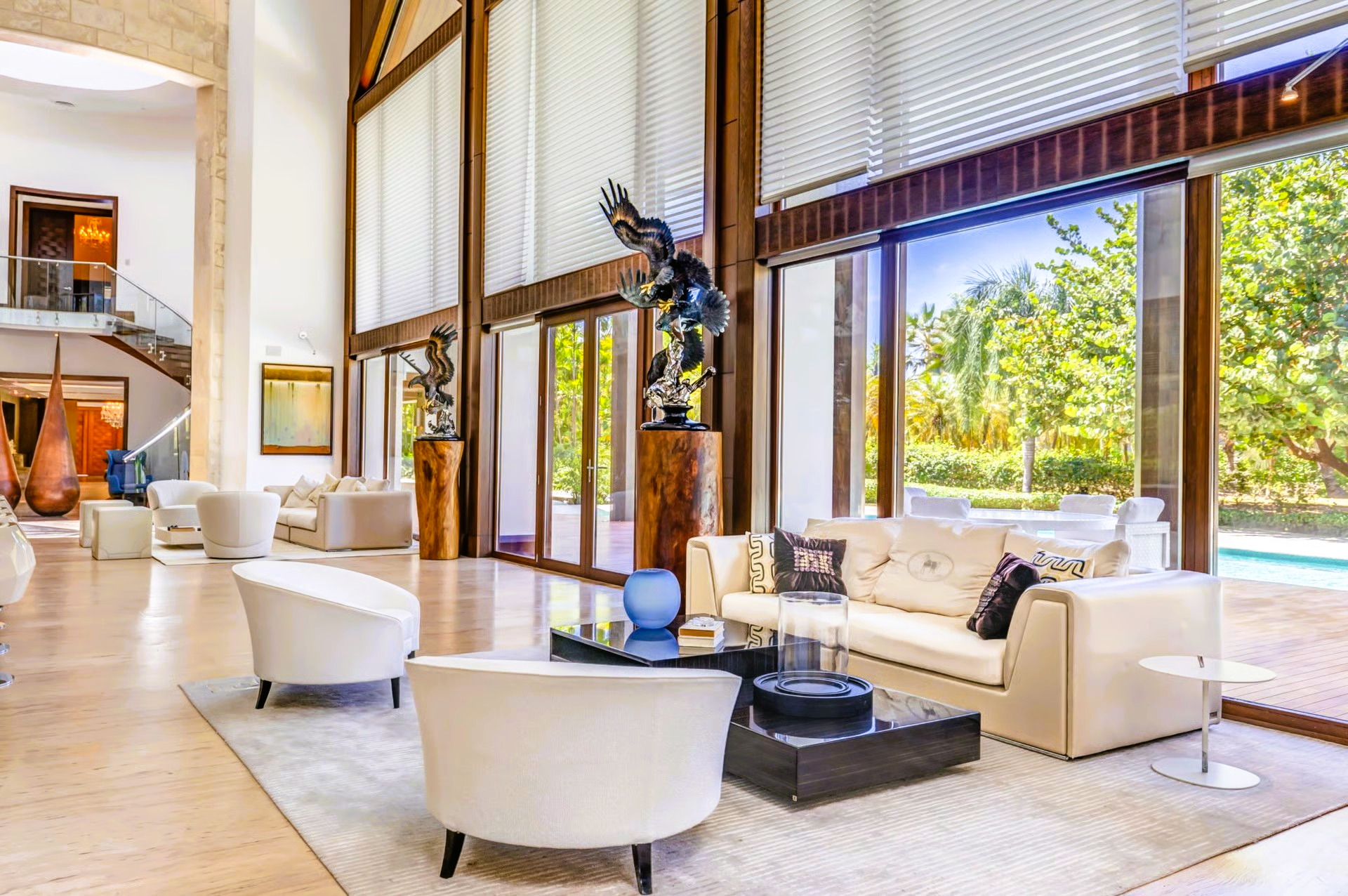Spacious modern living room with sculptures, sofas, and large windows overlooking a pool.