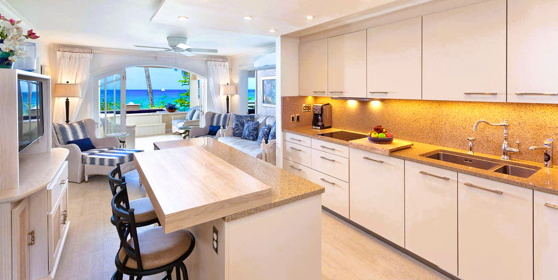 Bright, white kitchen with an open view to a beachfront living space; includes a breakfast bar with barstools.