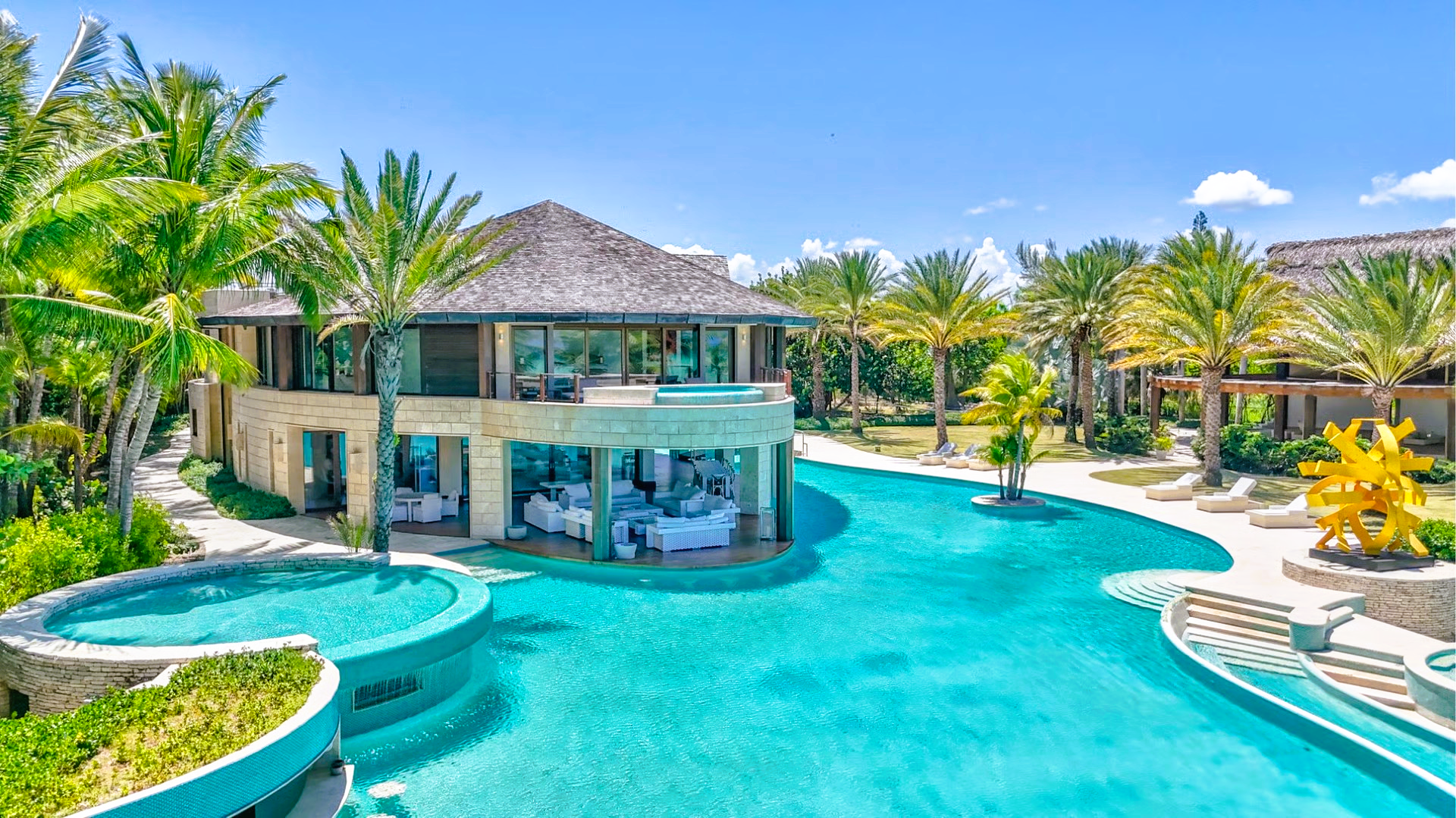 Luxury villa with a pool in a tropical setting. Blue water, palm trees, sunny day.