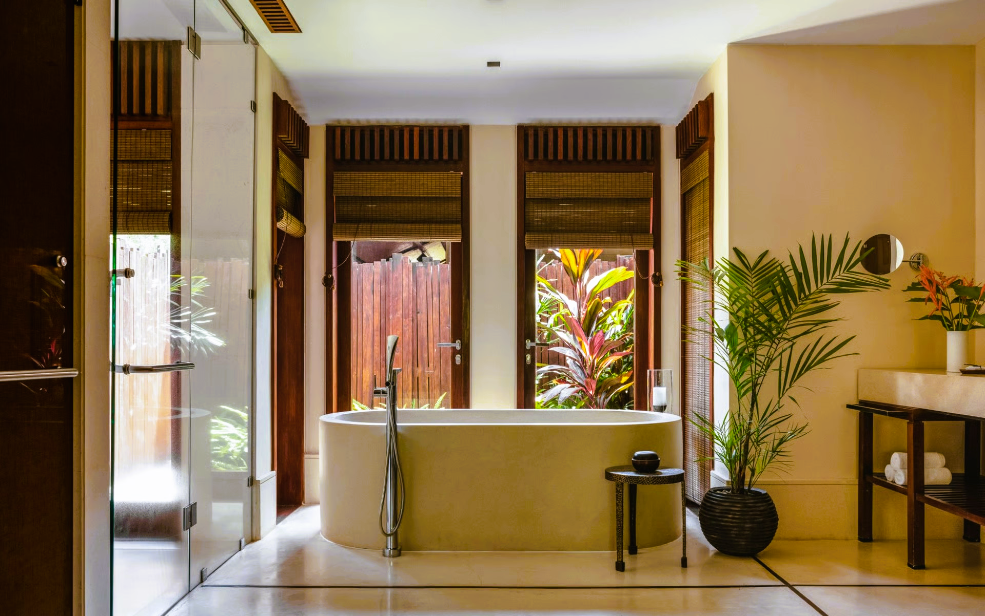 Bathroom with freestanding beige tub, open windows, and plants.