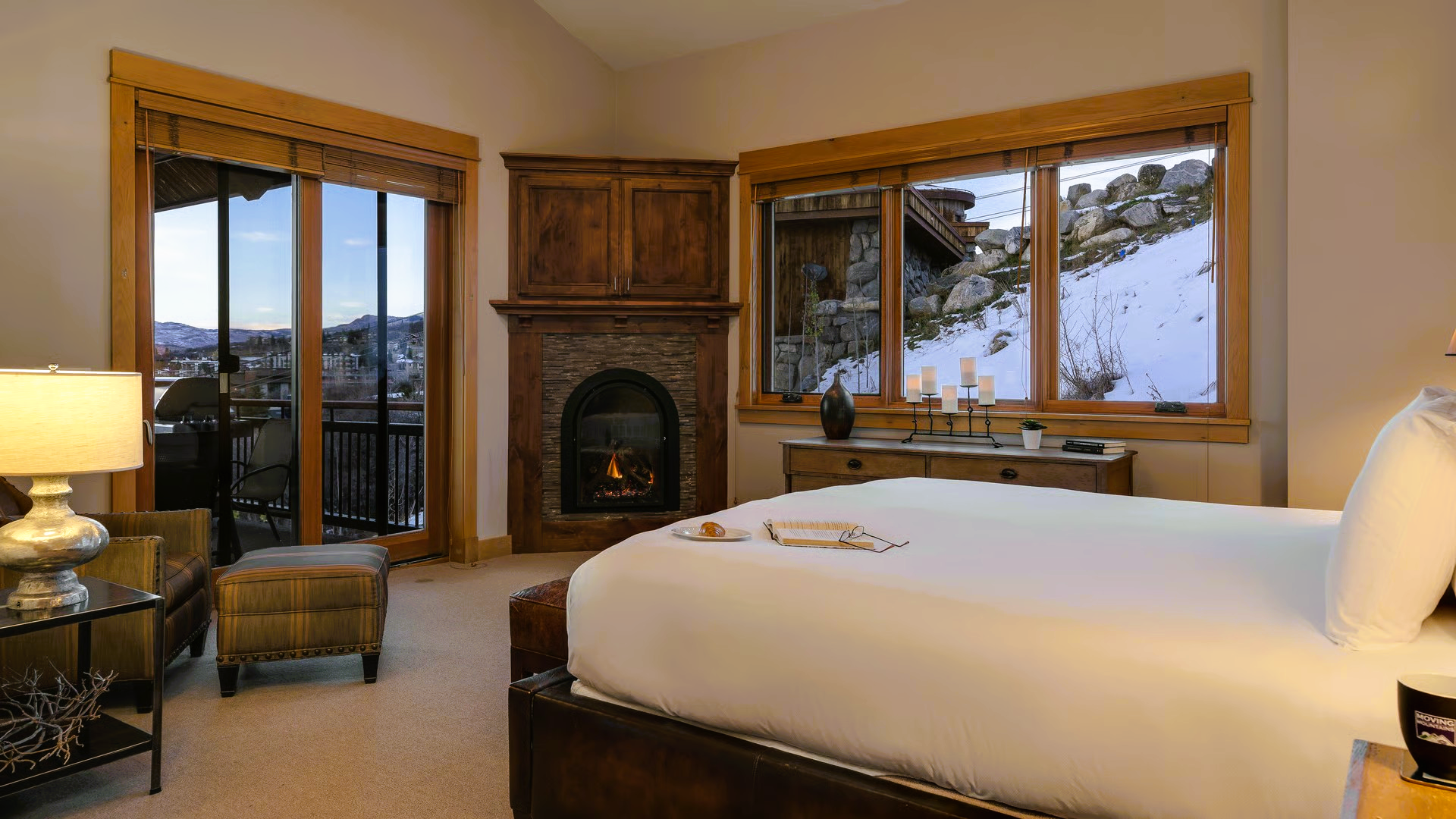 Cozy bedroom with a bed, fireplace, and windows overlooking a snowy landscape.