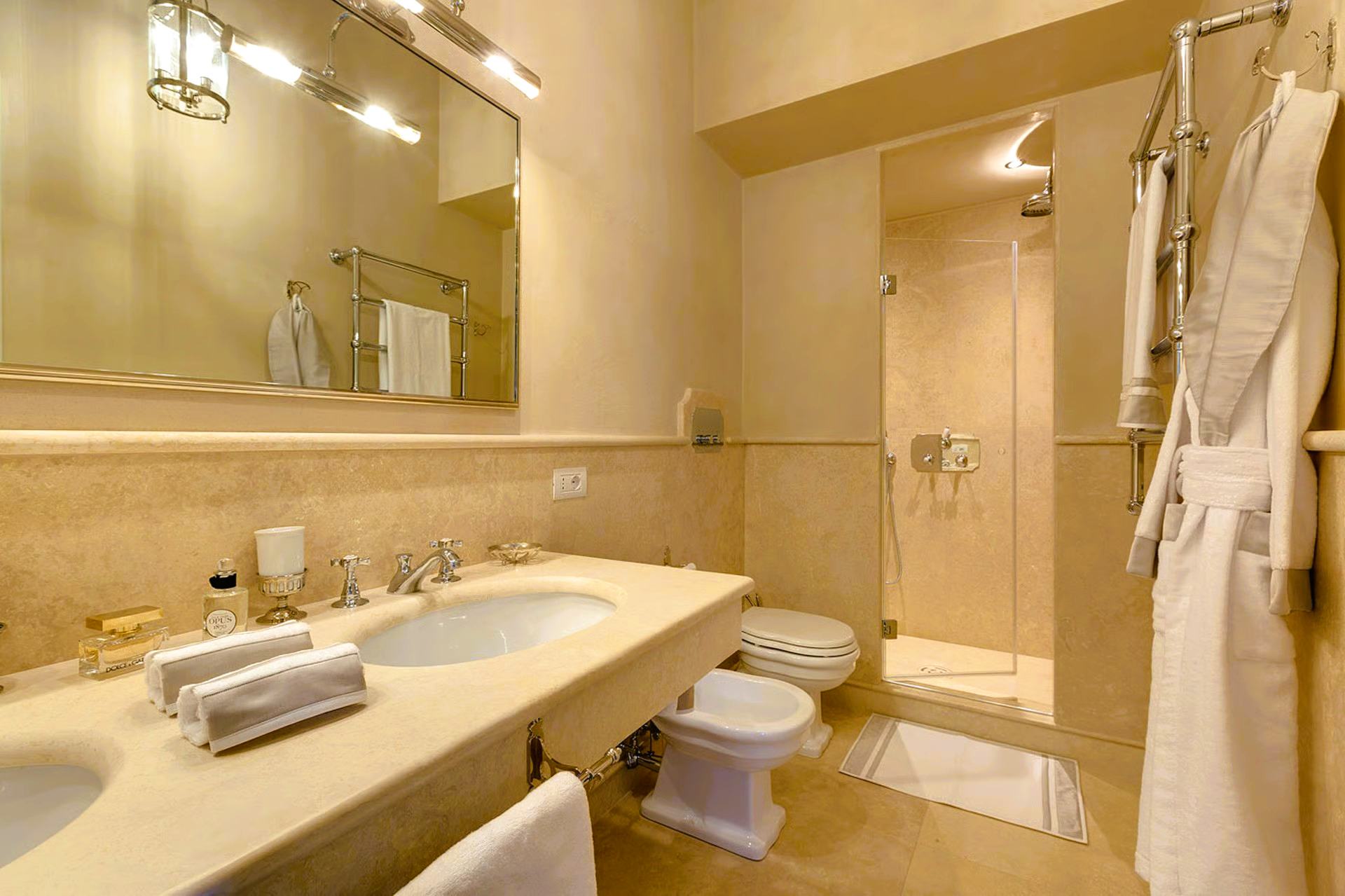 Bathroom with marble counter, double sinks, shower, and a bathrobe.