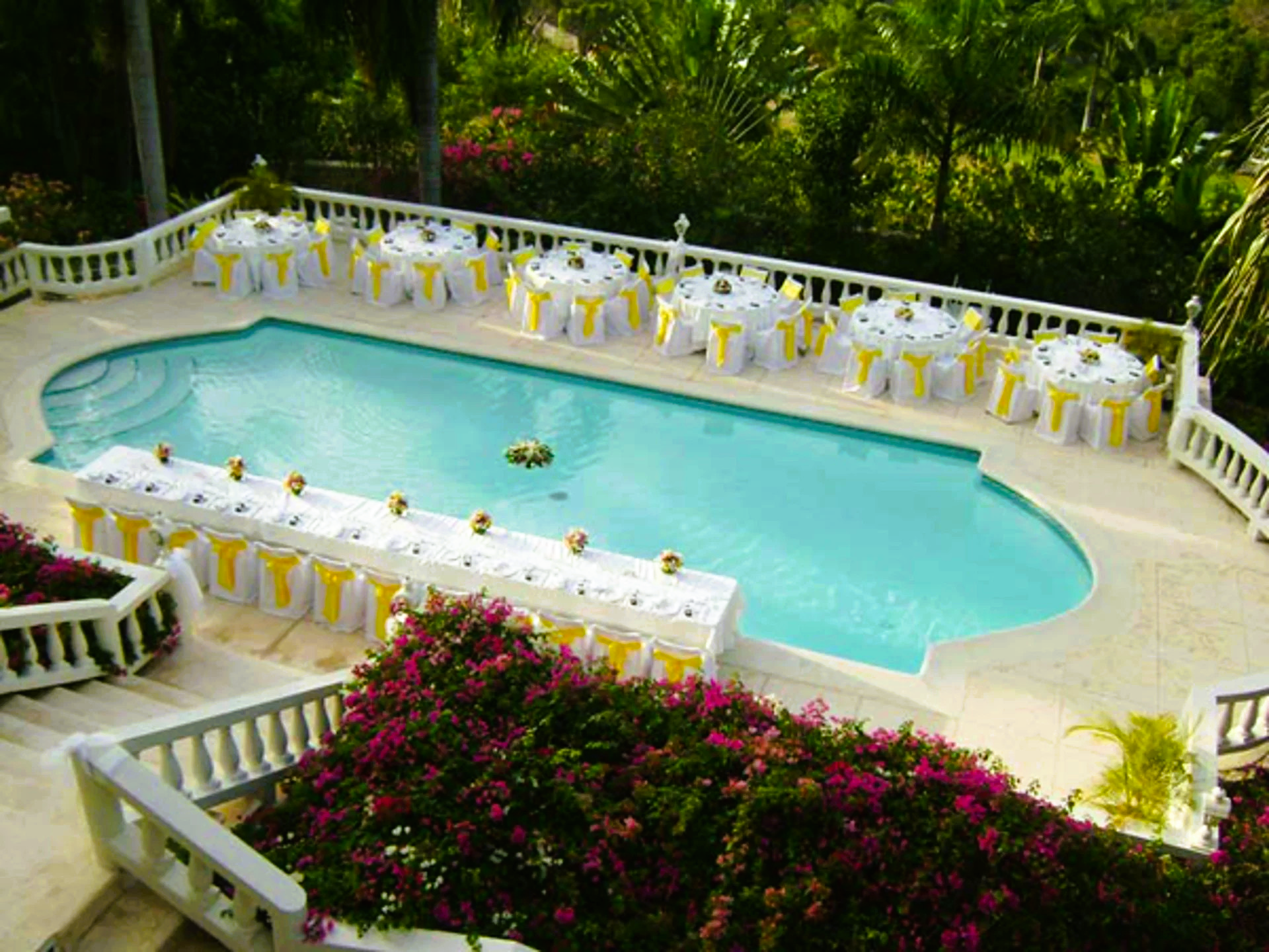 Poolside wedding reception with tables set up around the pool. Bougainvillea in bloom and lush green surroundings.