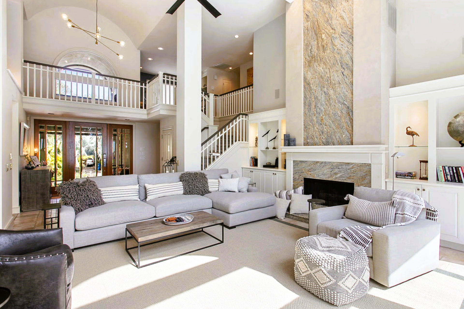 Spacious living room with high ceilings, light gray sectional, fireplace, and a balcony.