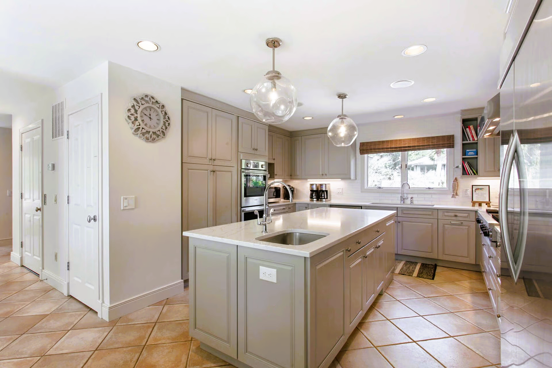 Modern kitchen with a large island, gray cabinets, and tiled floor.