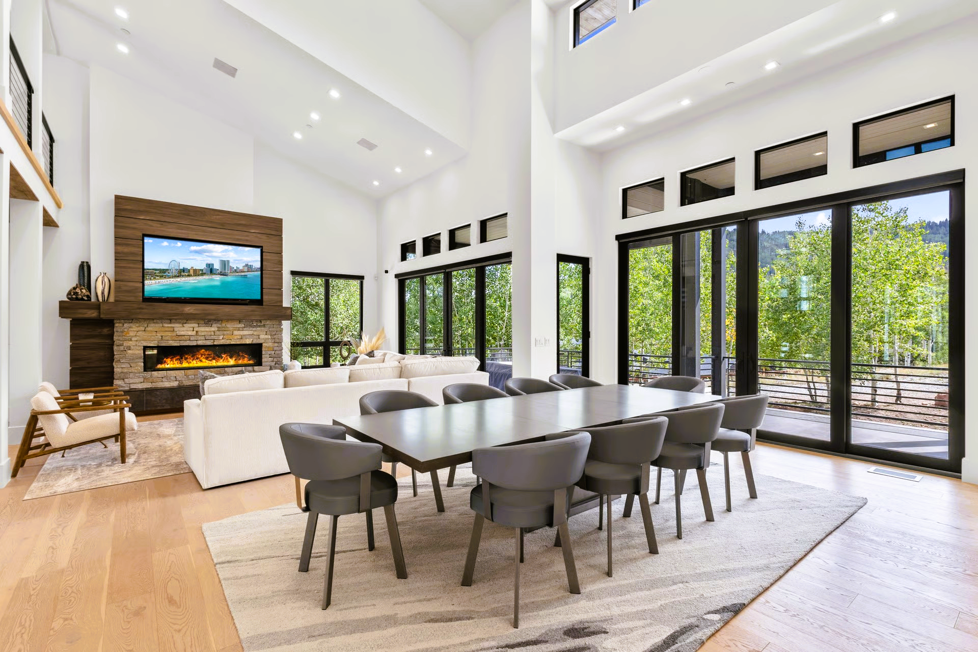 Spacious modern dining and living area with large windows, fireplace, and long table with chairs.
