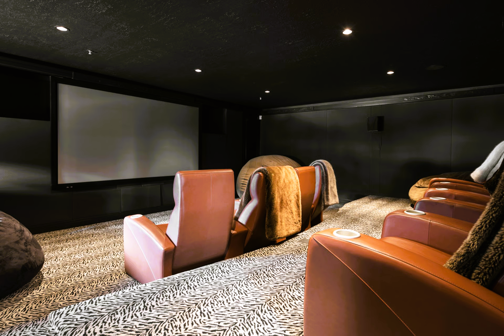 Home theater with brown leather recliners, large screen, dark walls, and patterned carpet.