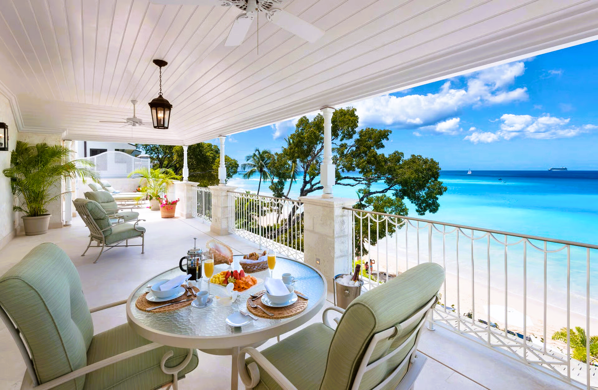 Balcony with breakfast table, ocean view, white sand beach, turquoise water, blue sky.