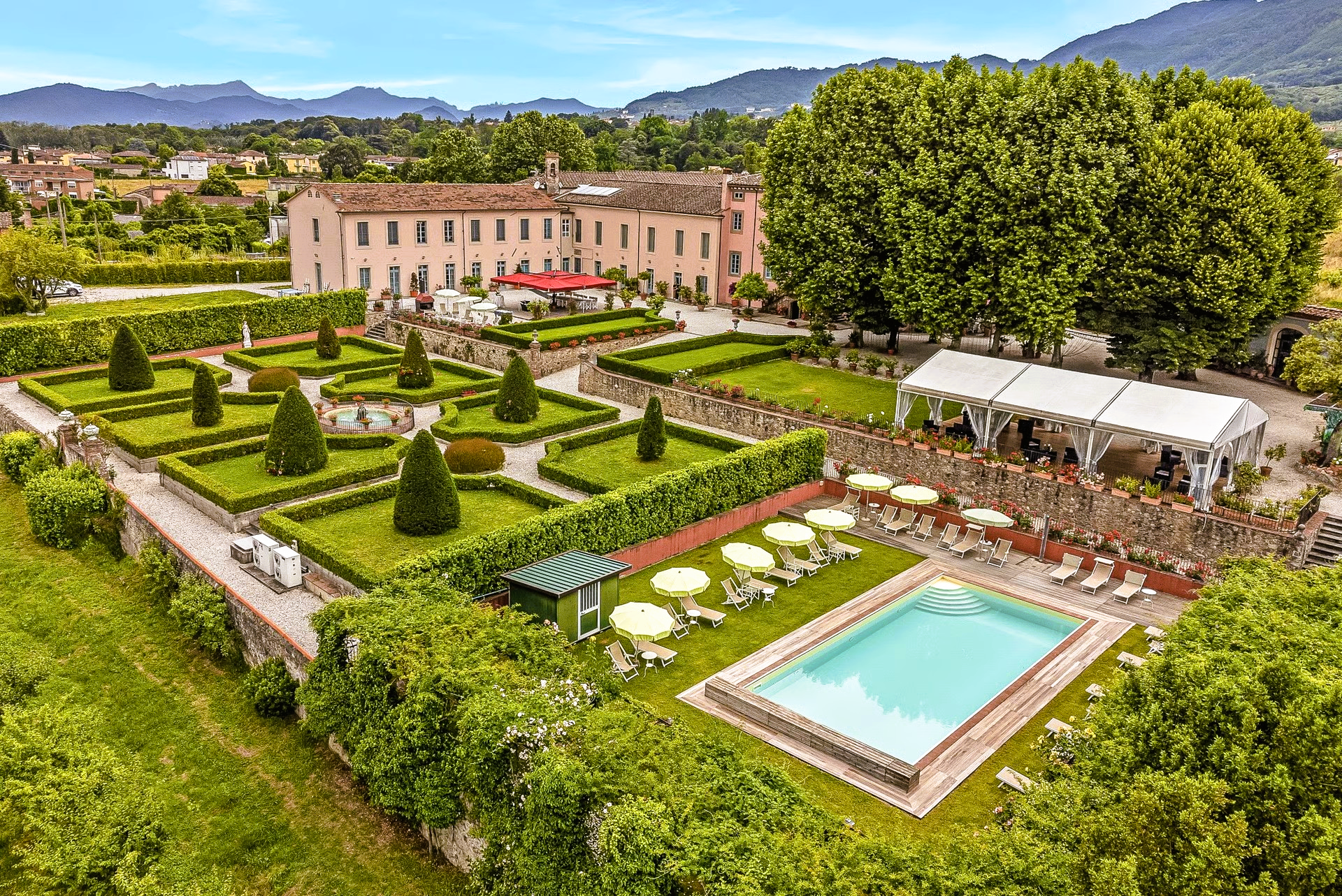 Luxury hotel with manicured gardens, a pool, and mountains in the background.