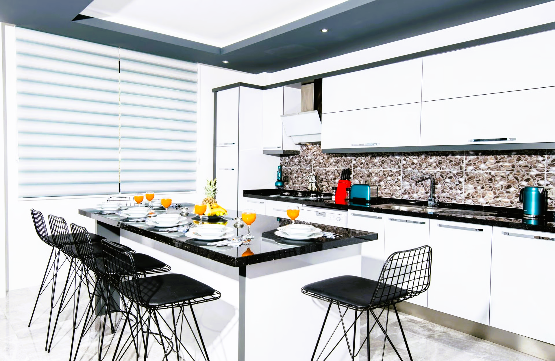 Modern kitchen with white cabinets, black countertops, island with seating, and black metal chairs.