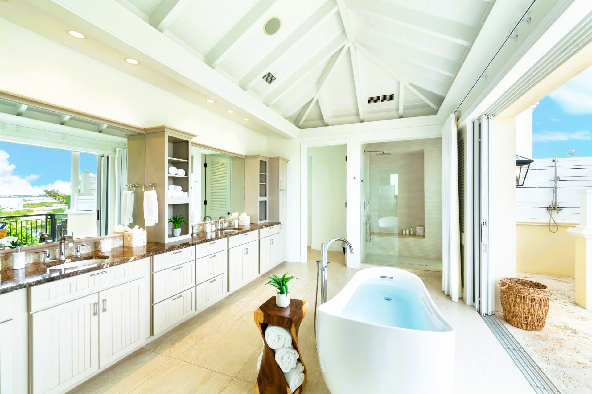 Bright white luxury bathroom with a soaking tub, vanity, and open access to a balcony with a view.