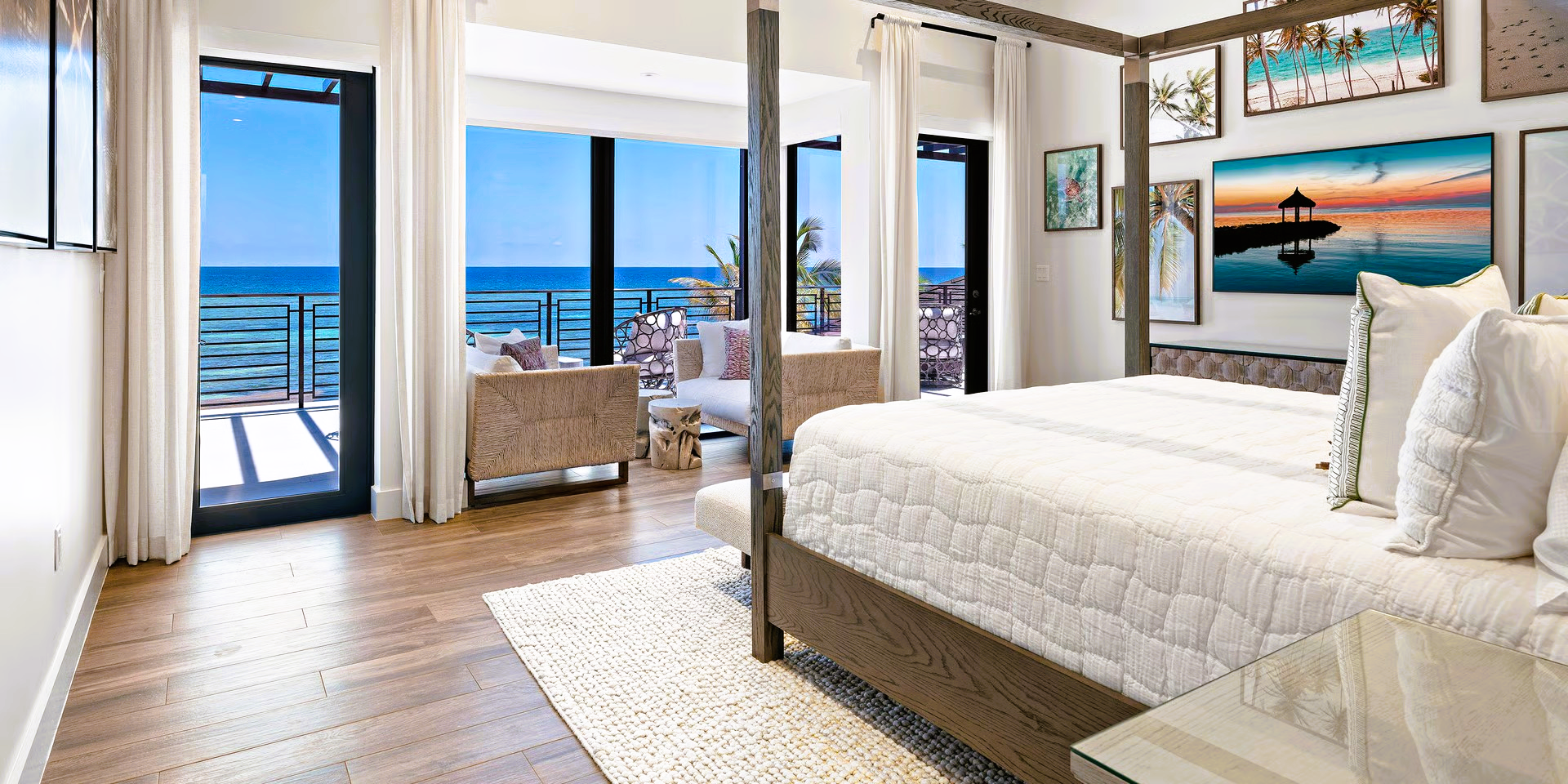 Bedroom with a view of the ocean. Features a canopy bed, hardwood floors, large windows, and art on the wall.