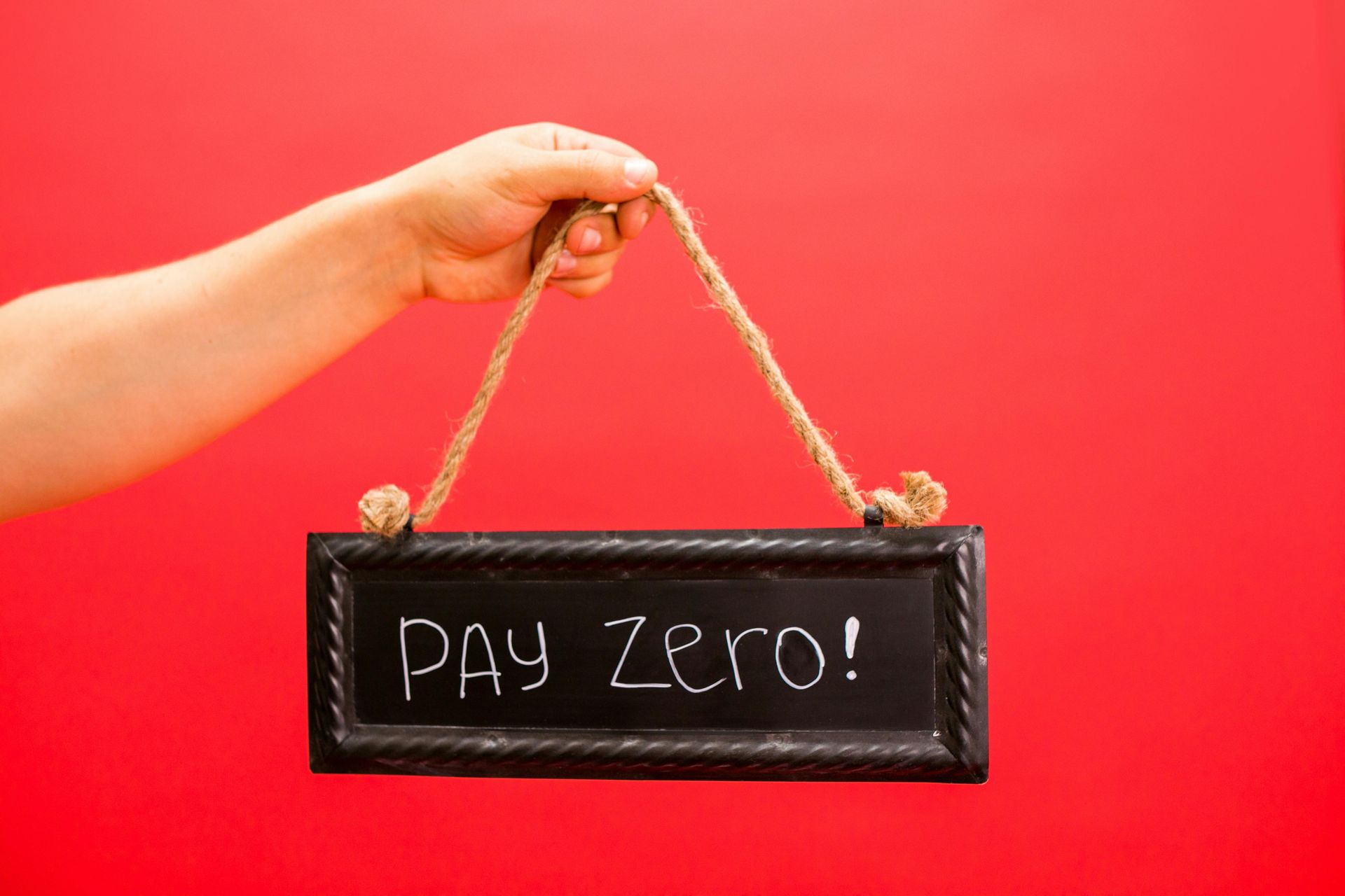 Hand holding a black sign that says "Pay Zero!" against a red background.