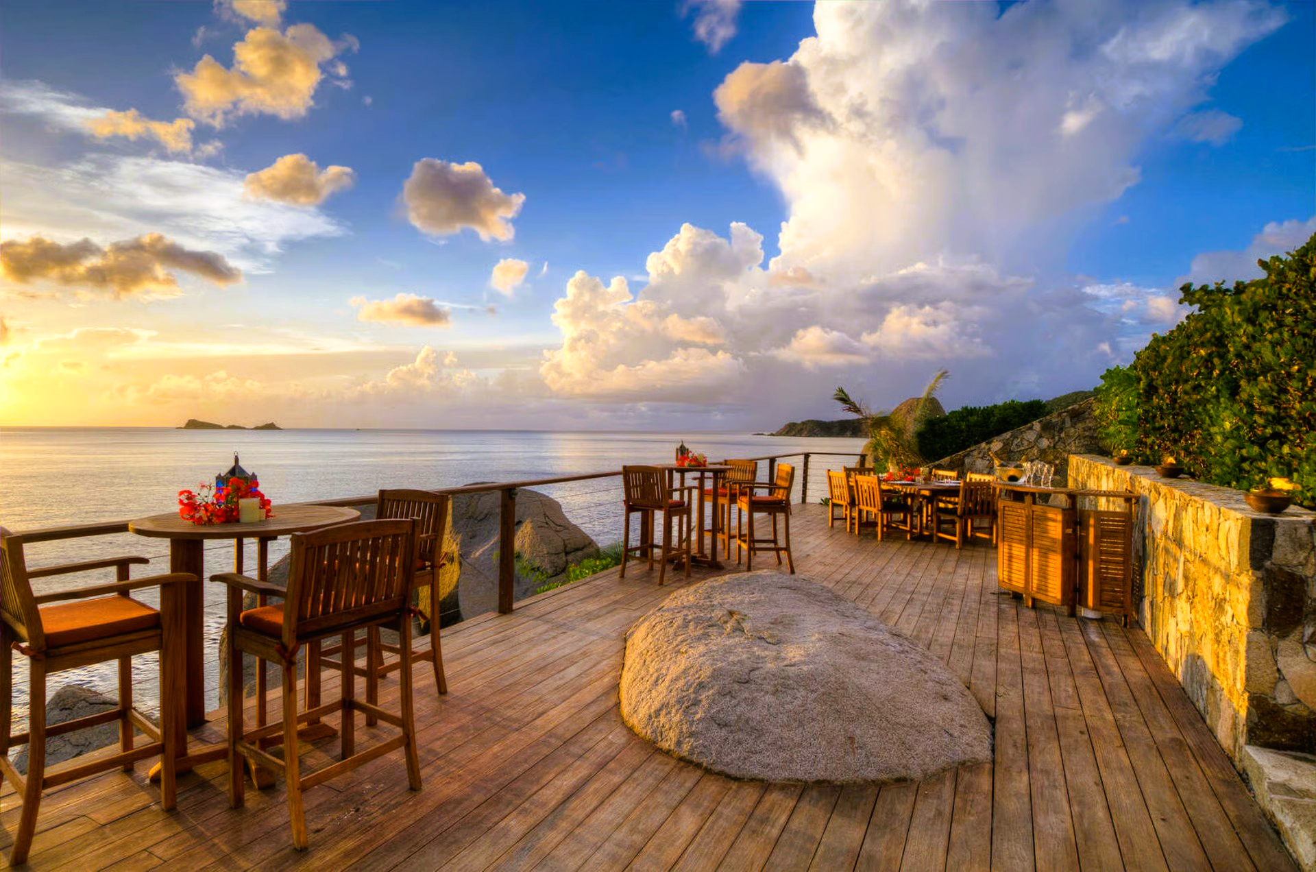 Wooden deck with tables and chairs overlooking ocean at sunset.