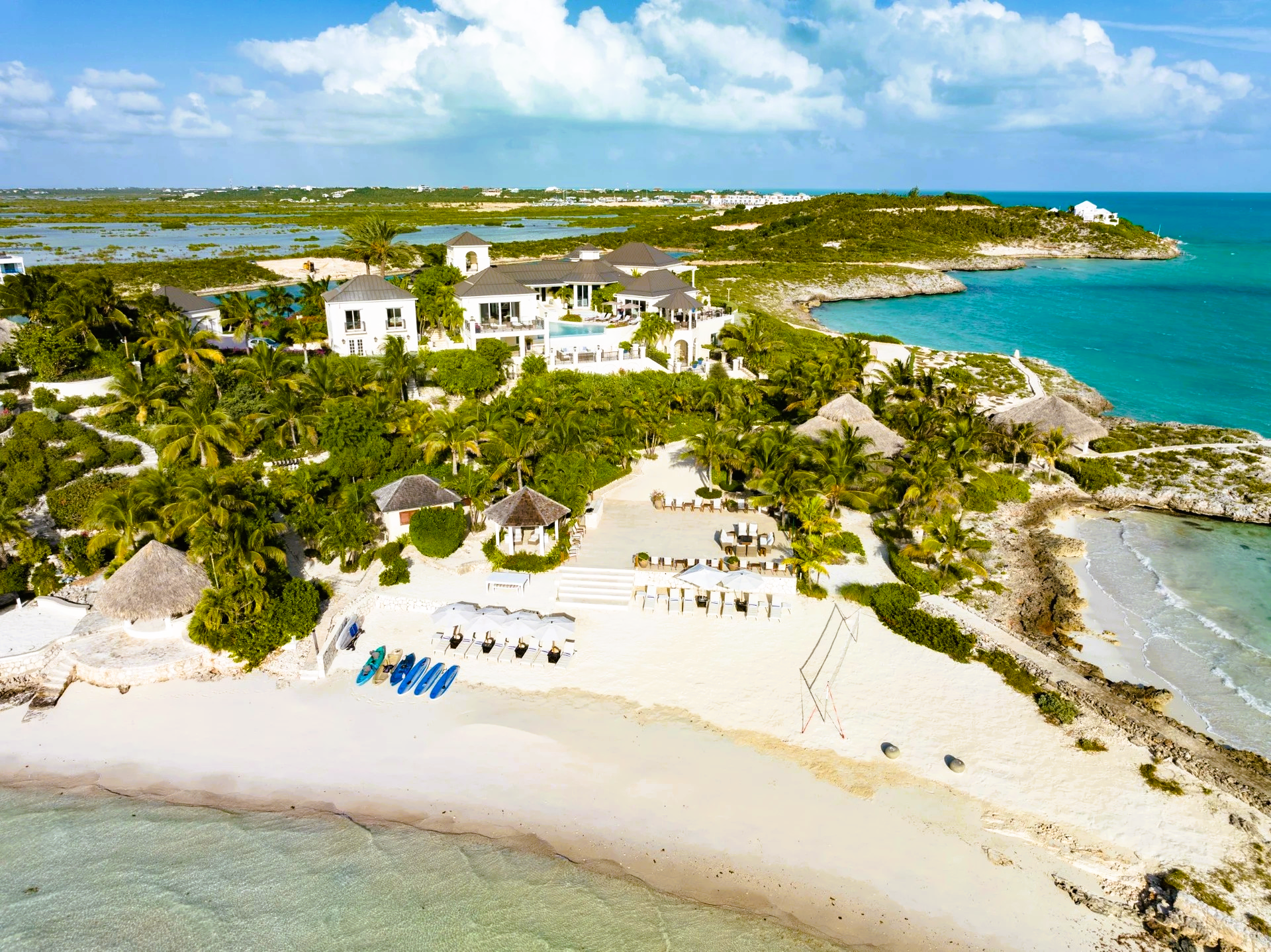 Aerial view of a luxurious beachfront property with white sand, turquoise water, and lush green vegetation.