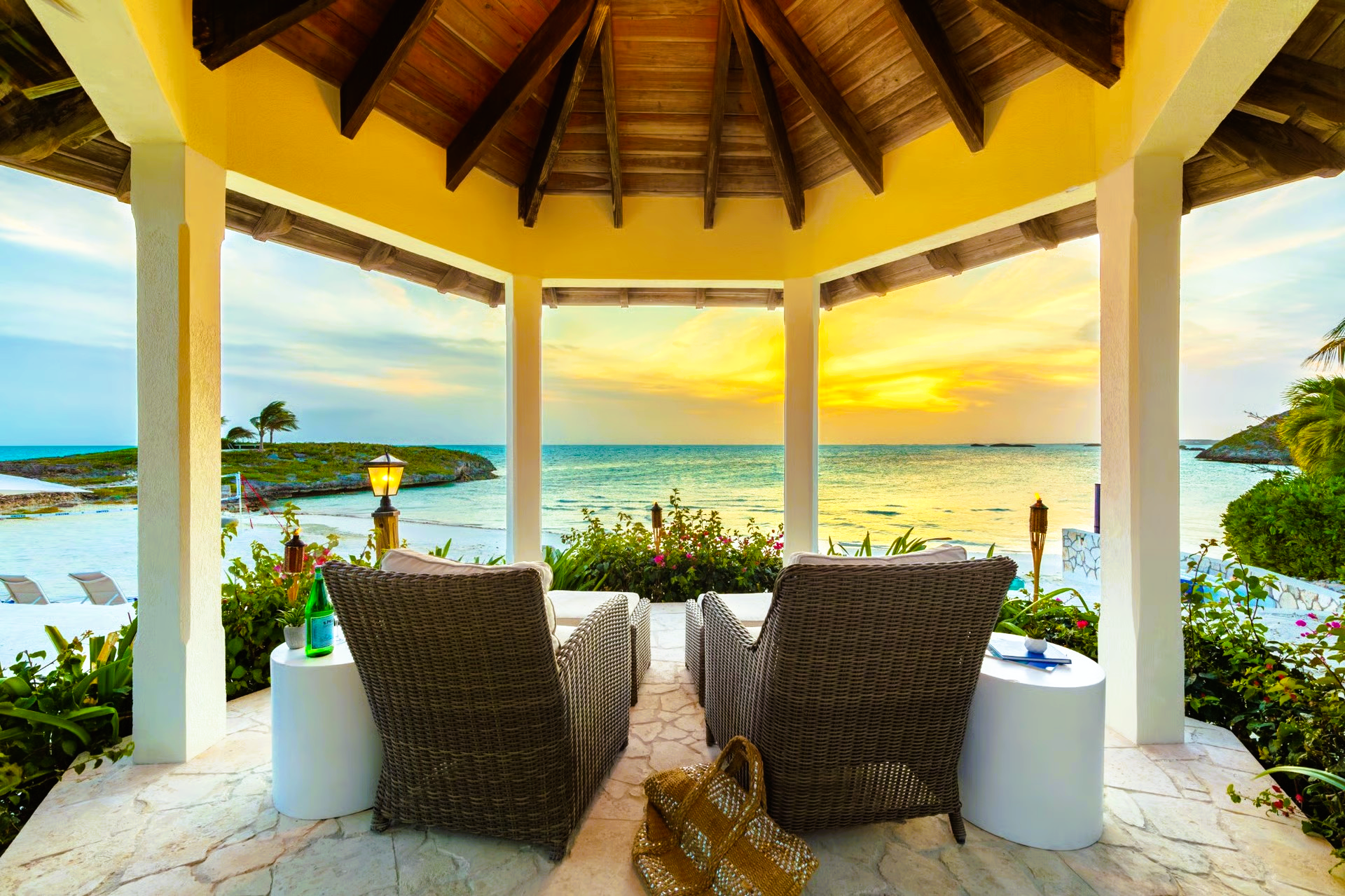 Gazebo with wicker chairs facing ocean at sunset.