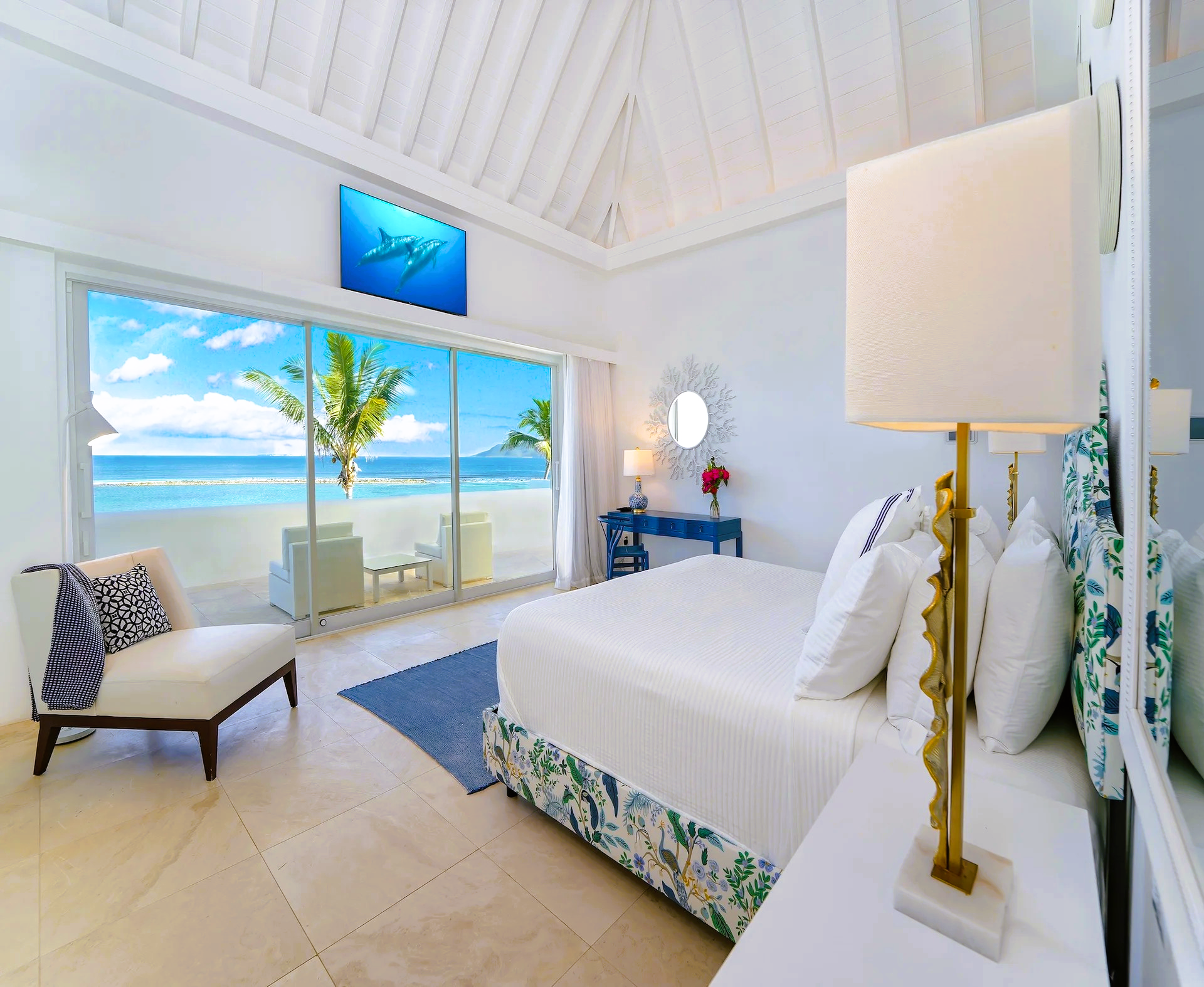 Bright white bedroom with a beach view, a large bed, and a lounge chair.