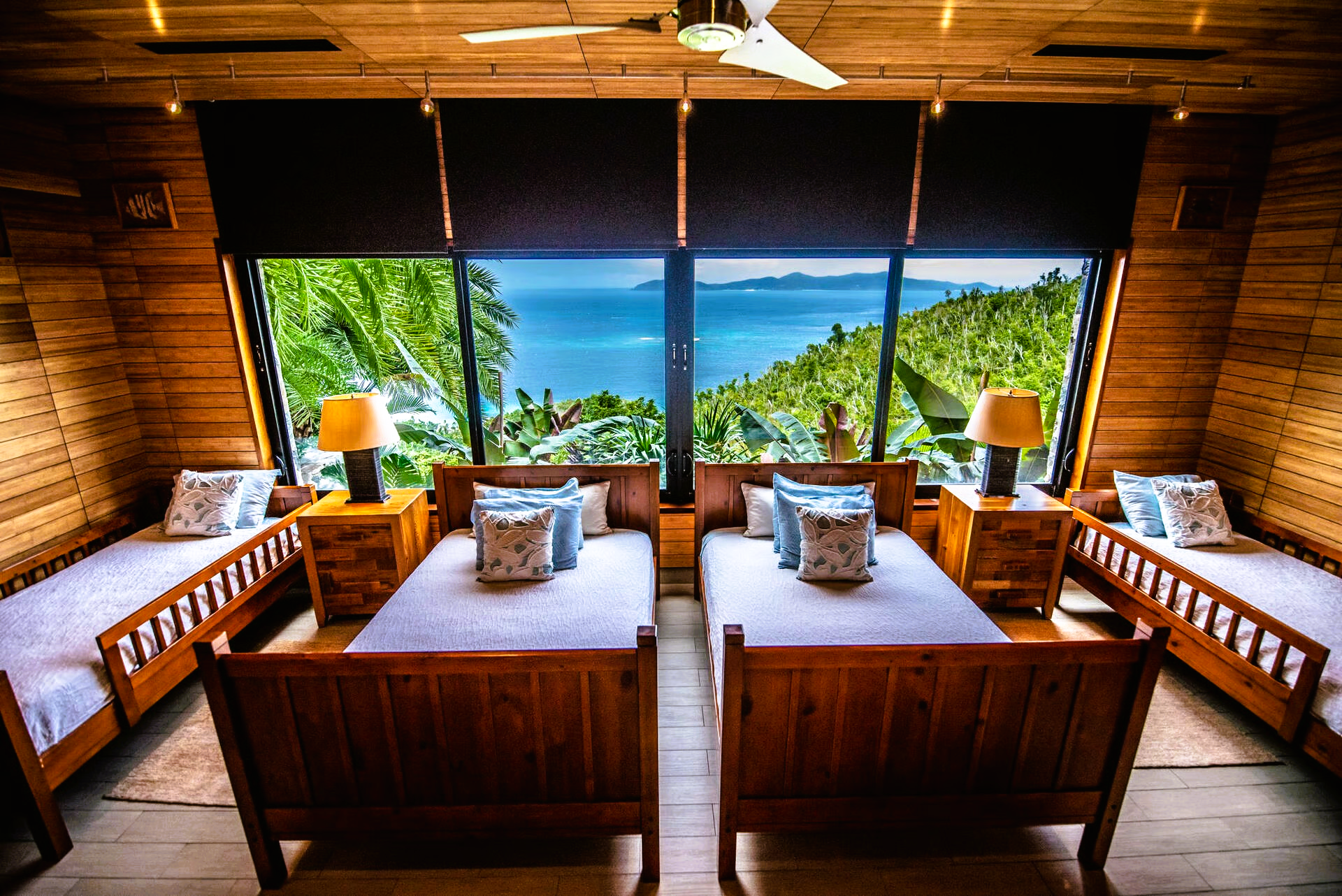 Bedroom with wooden furniture, large windows overlooking a tropical ocean view.